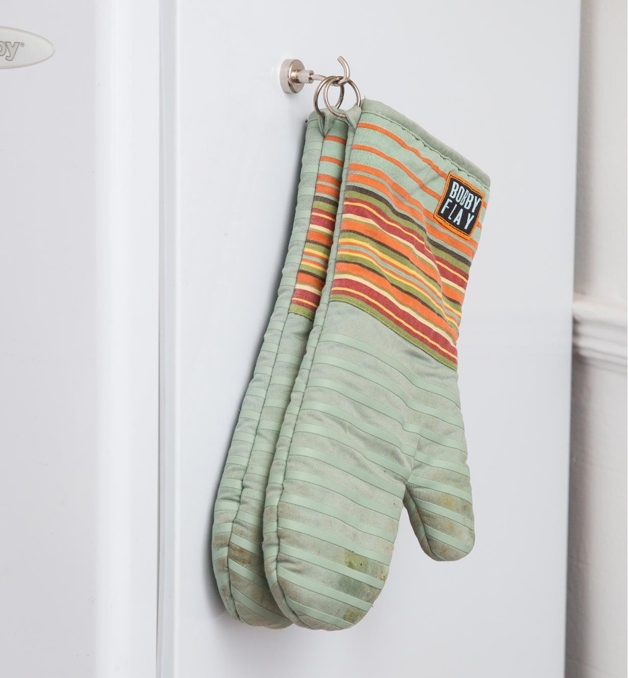 Oven mitts hanging on a magnet-mounted hook attached to a fridge