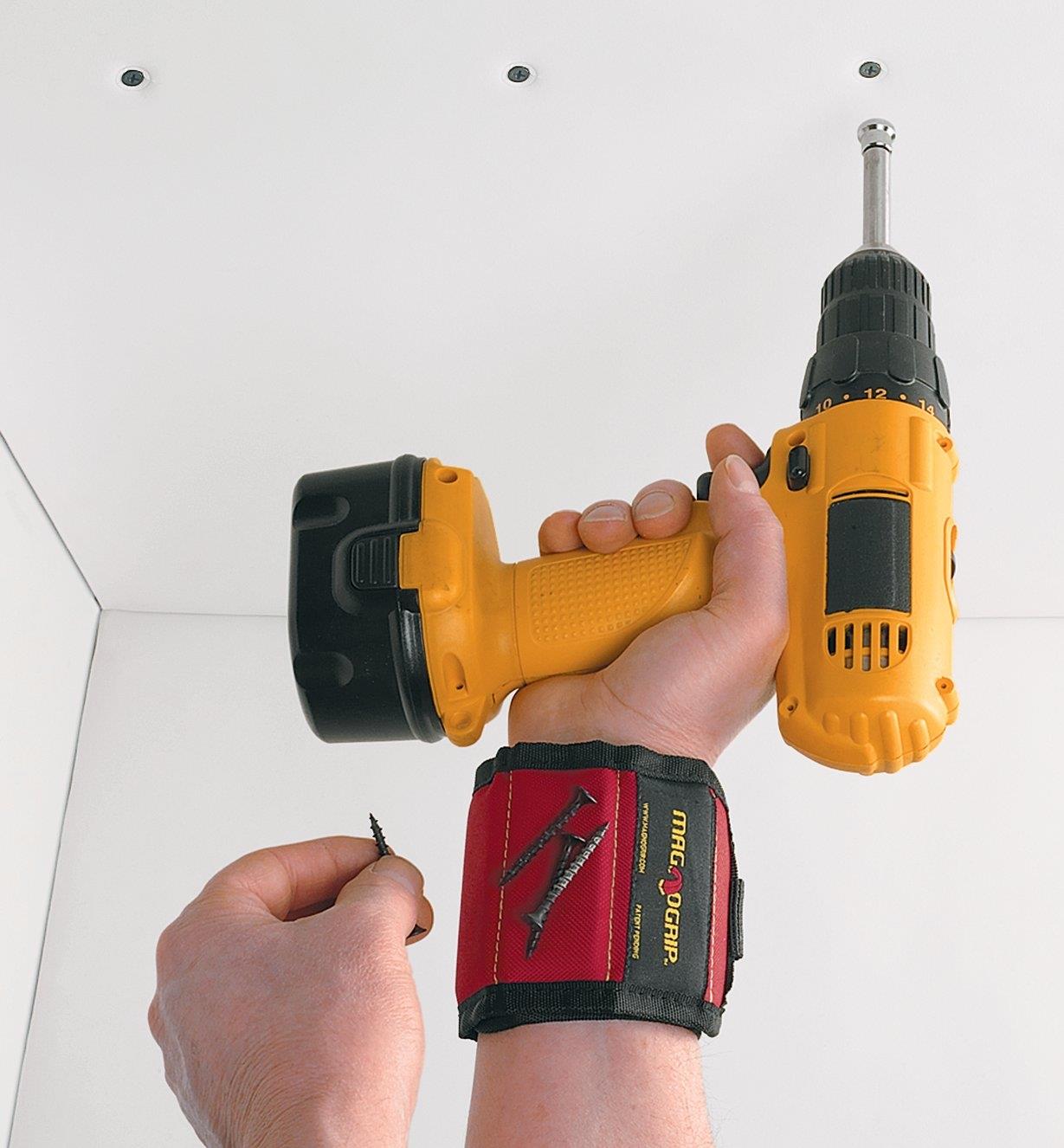 Holding a cordless drill while wearing a wrist nail holder with screws magnetically attached to it