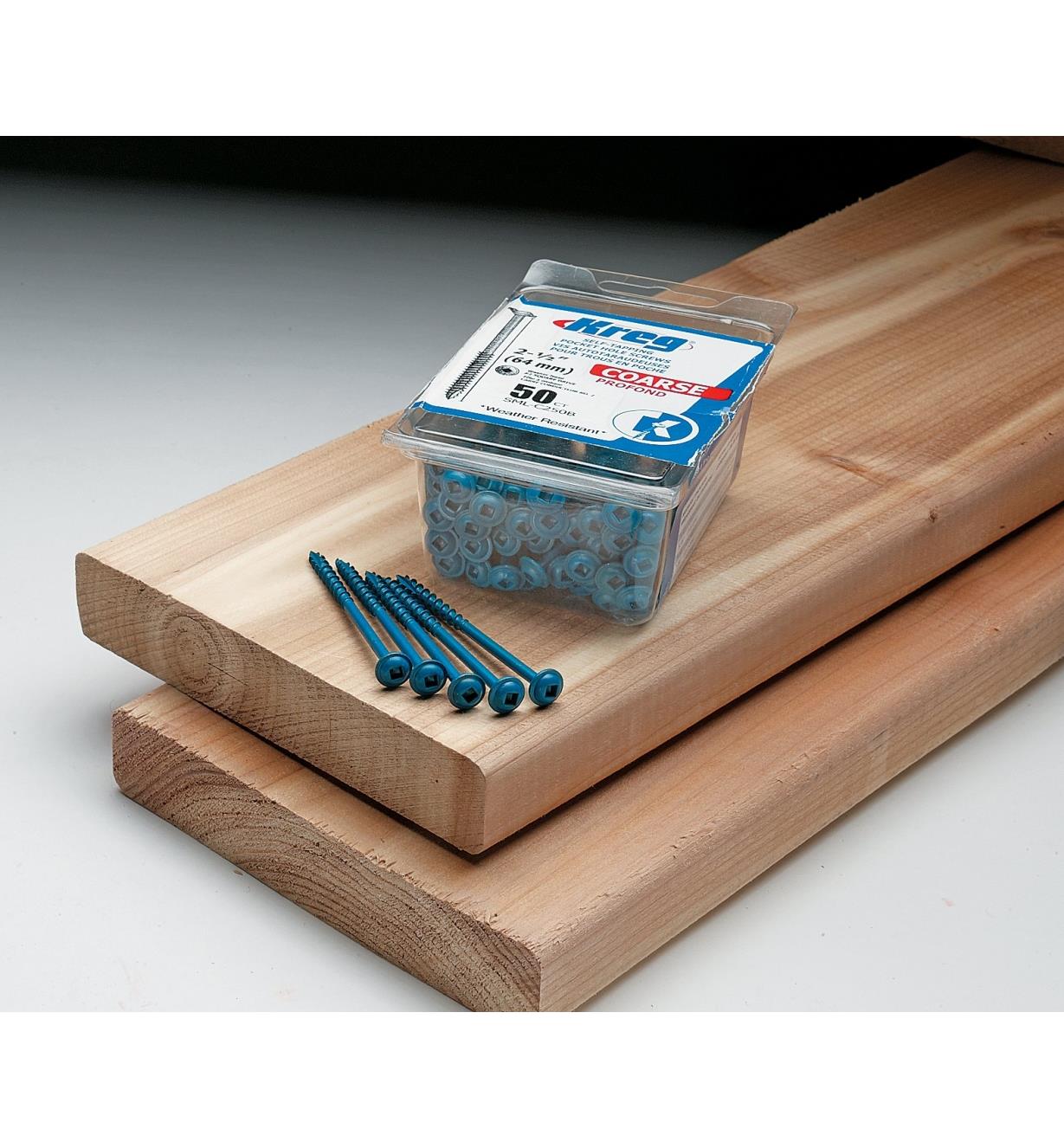 Box of Blue-Kote screws sitting on two deck boards beside several screws