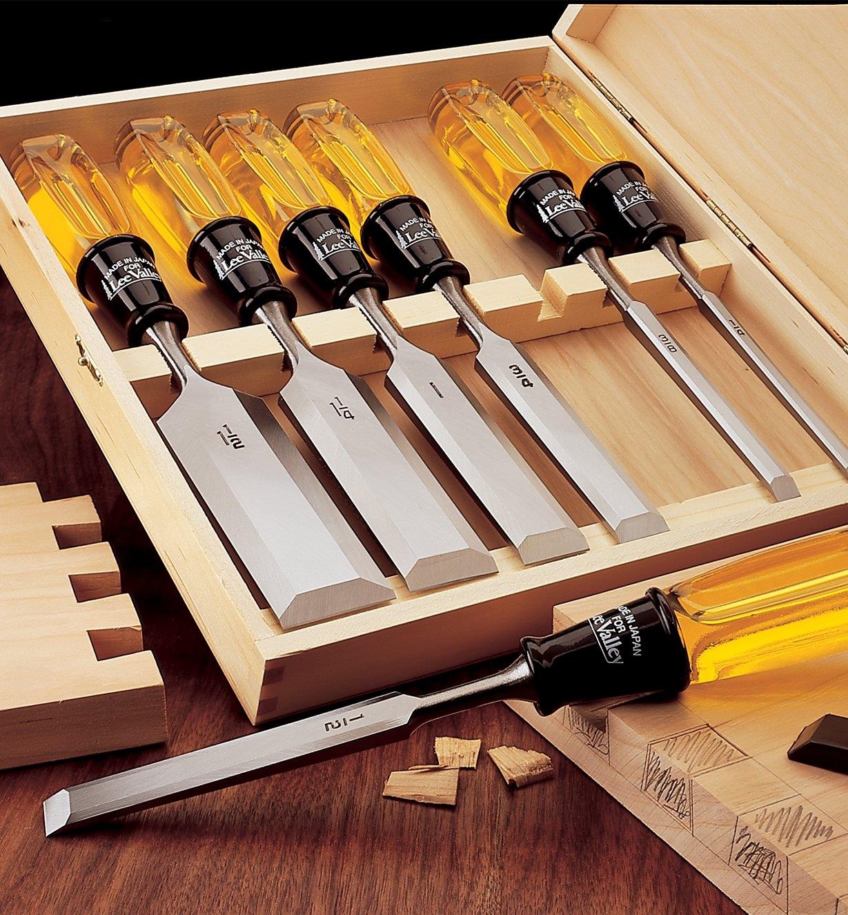Boxed Set of 7 Bevel-Edge Chisels sitting on a table beside boards that are being cut with dovetail joints