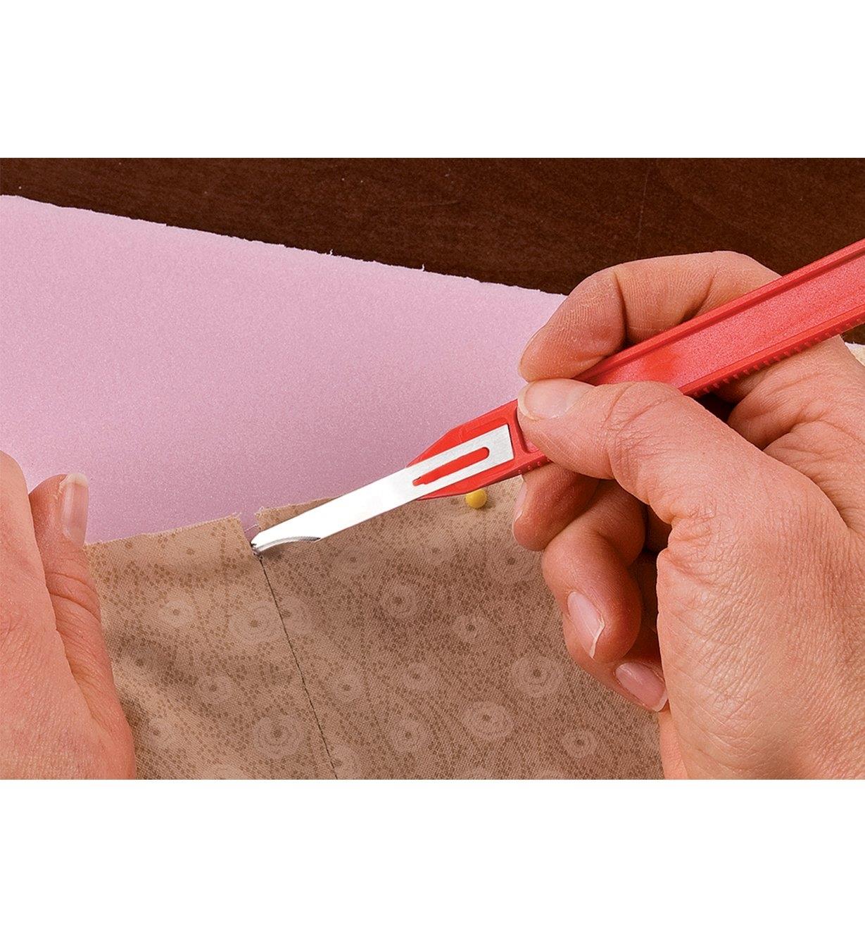 Personne utilisant un outil à découdre muni d'une lame à pointe tranchante pour défaire les premiers points d'une couture