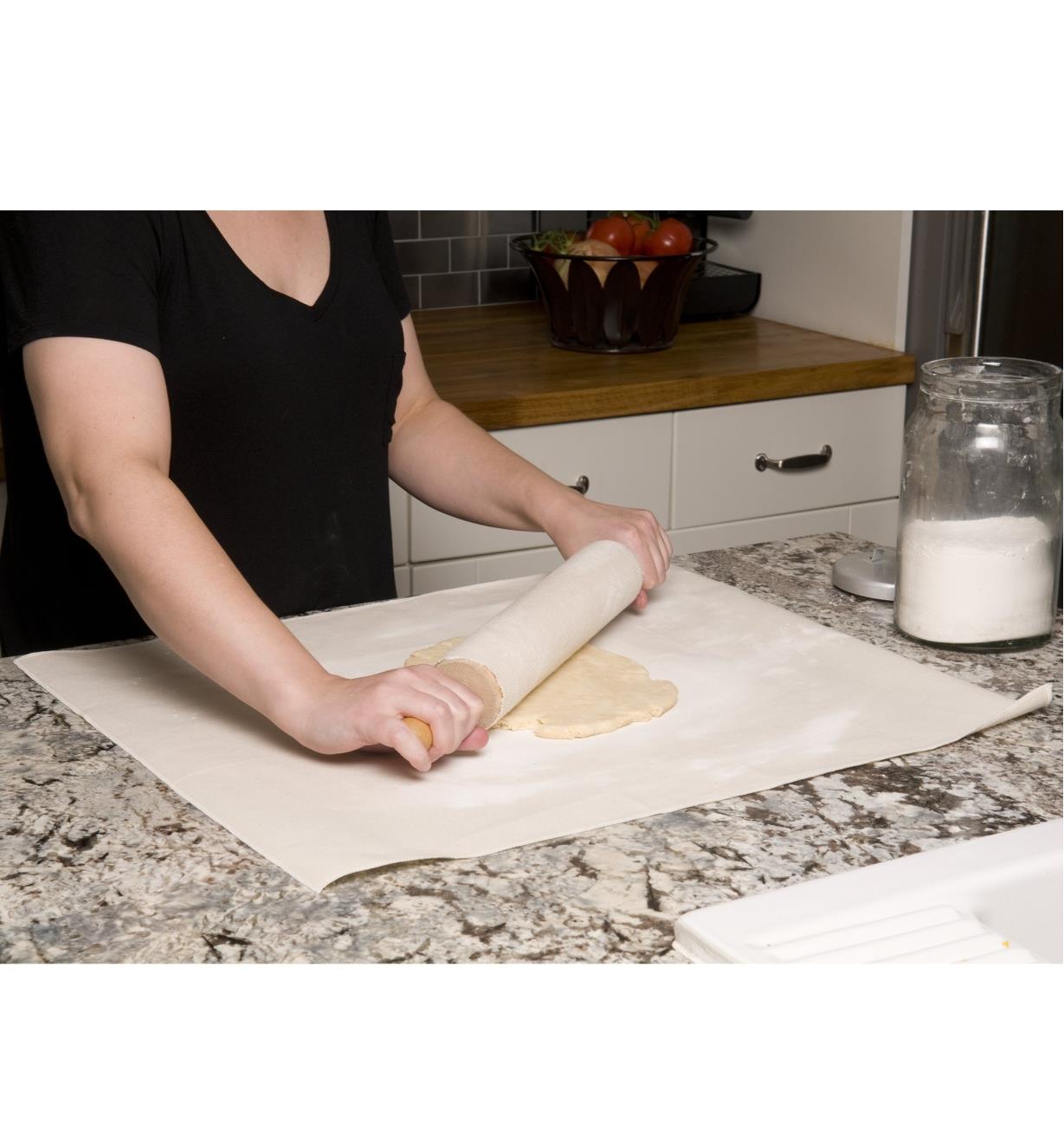 Rolling out dough on the pastry cloth using a rolling pin with a cover on it 