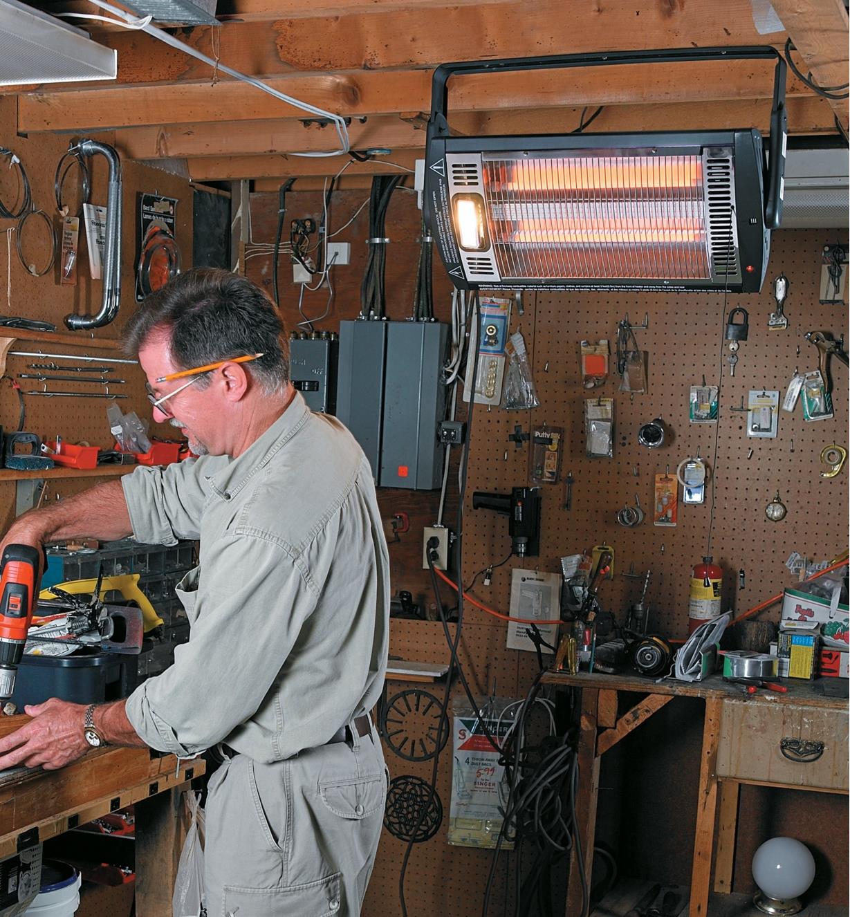 Person working in a workshop being warmed by a Quartz Overhead Radiant Heater suspended from the ceiling.