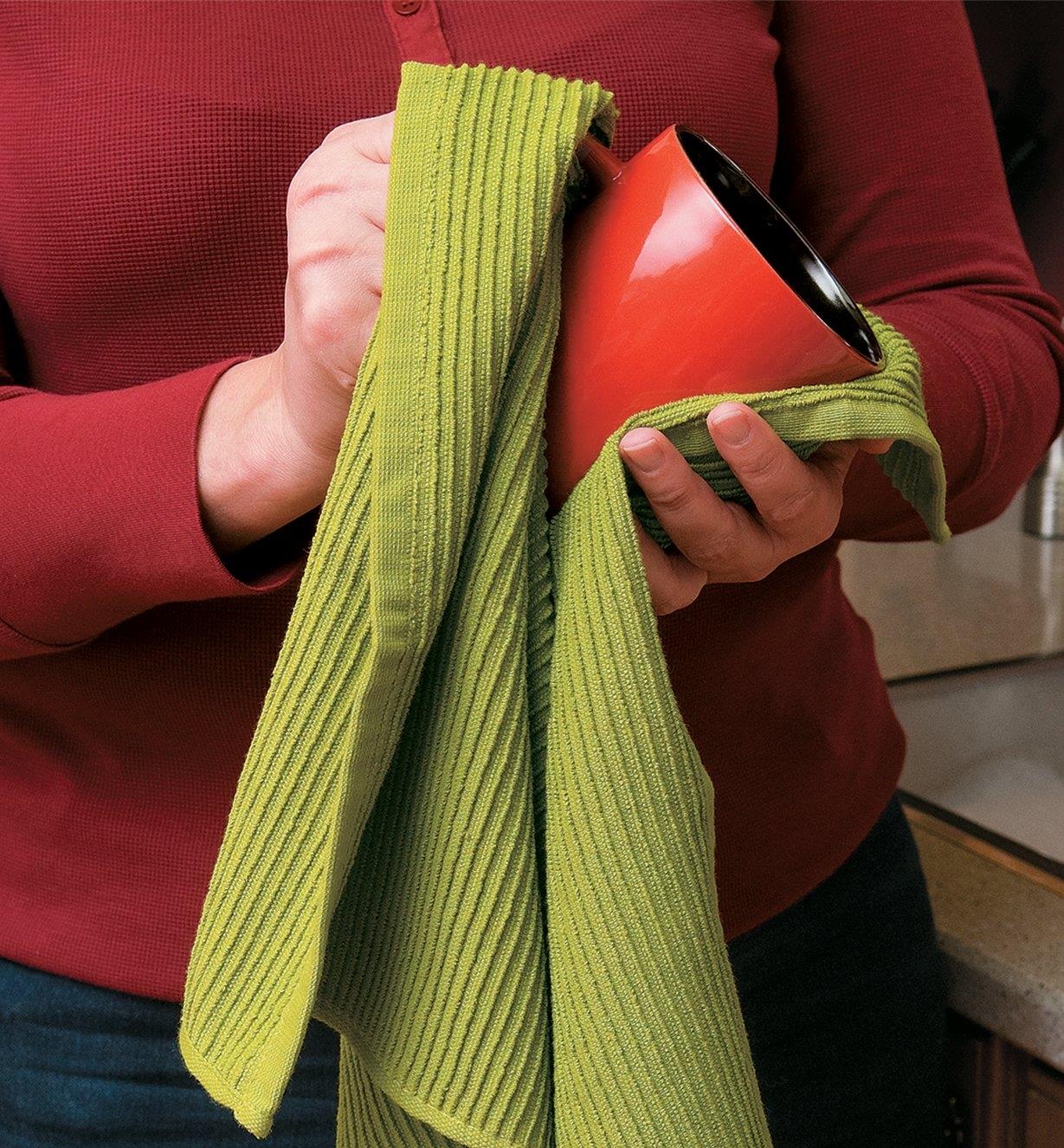 A woman drying a mug with a green ripple towel
