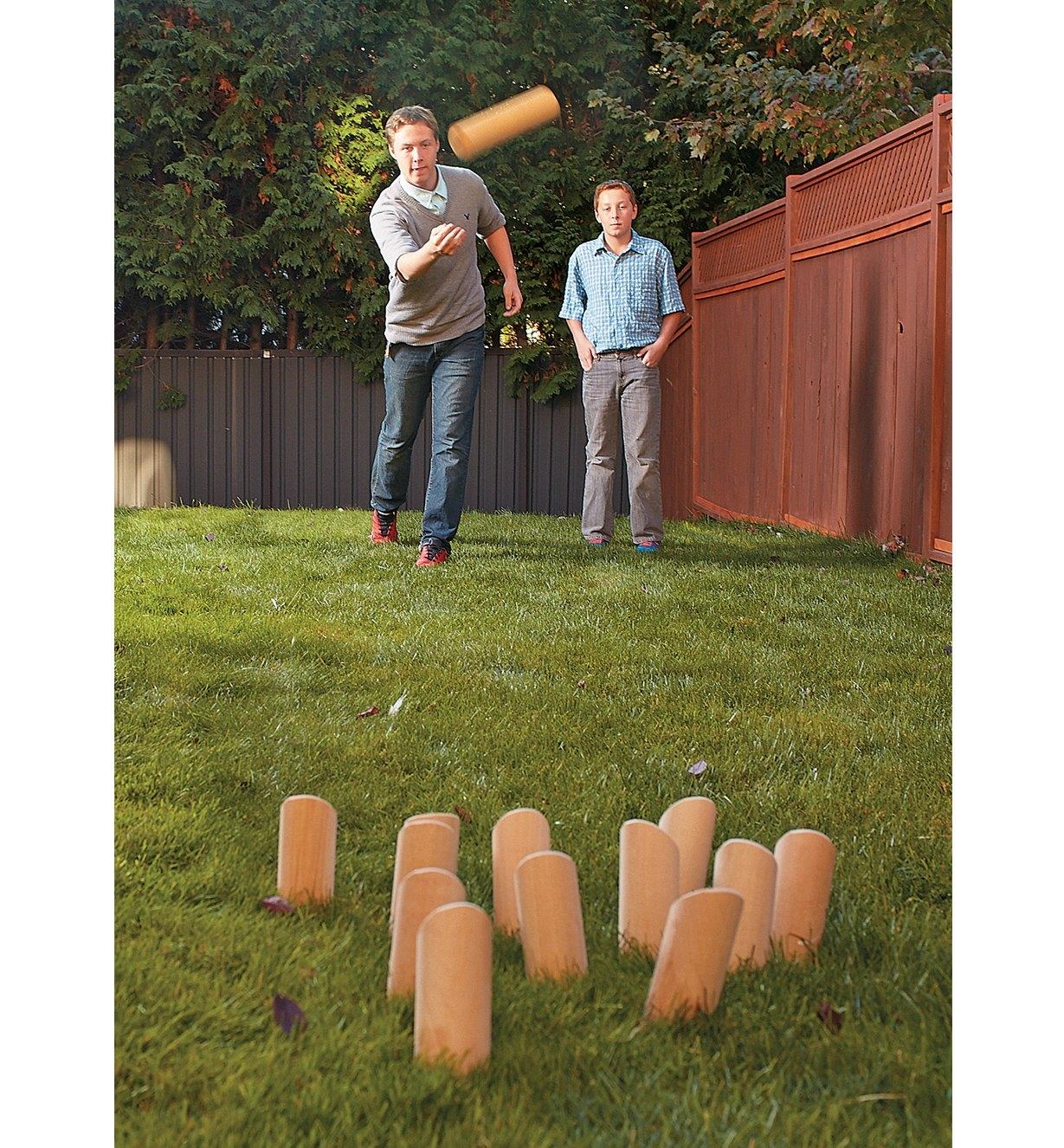 A man throws the mölkky toward the skittles while a boy watches