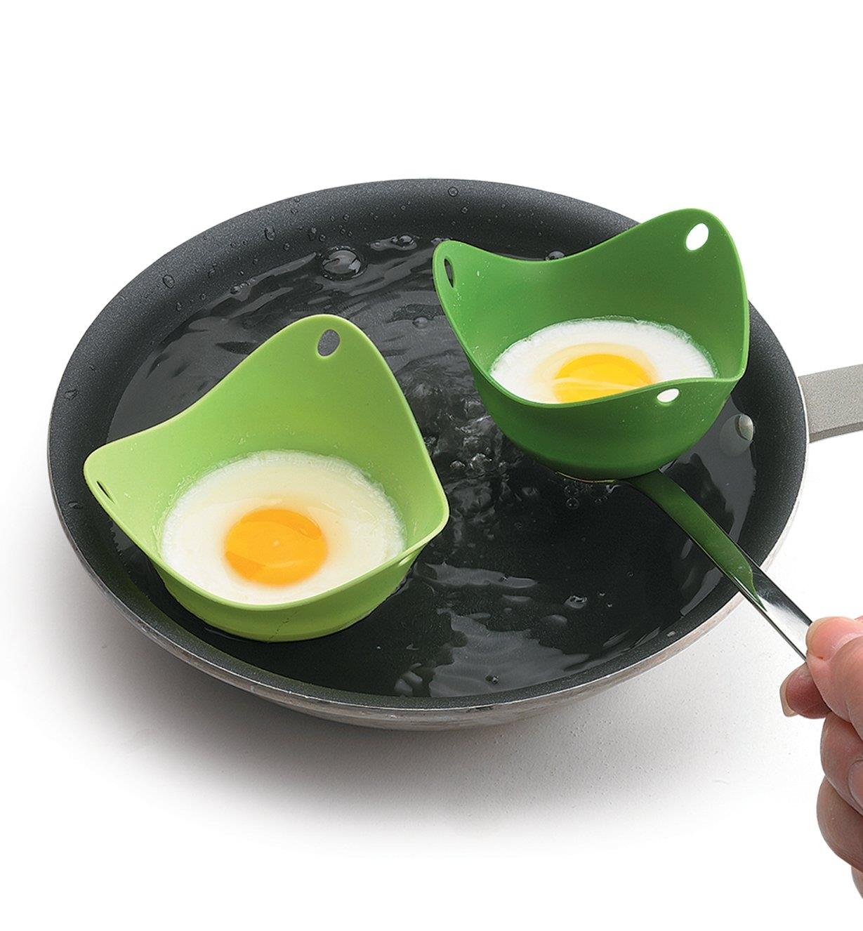 A pair of pods poaching eggs in a pan of boiling water
