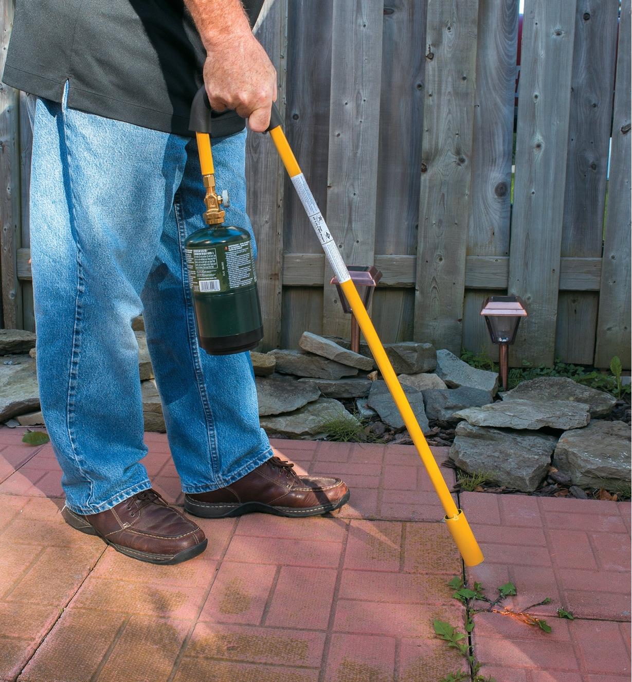 A man uses a Mini Weed Torch to remove weeds from a patio