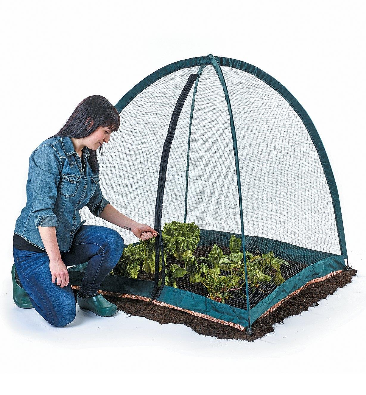 A woman unzips the Pop-Up Plant Dome covering a vegetable garden