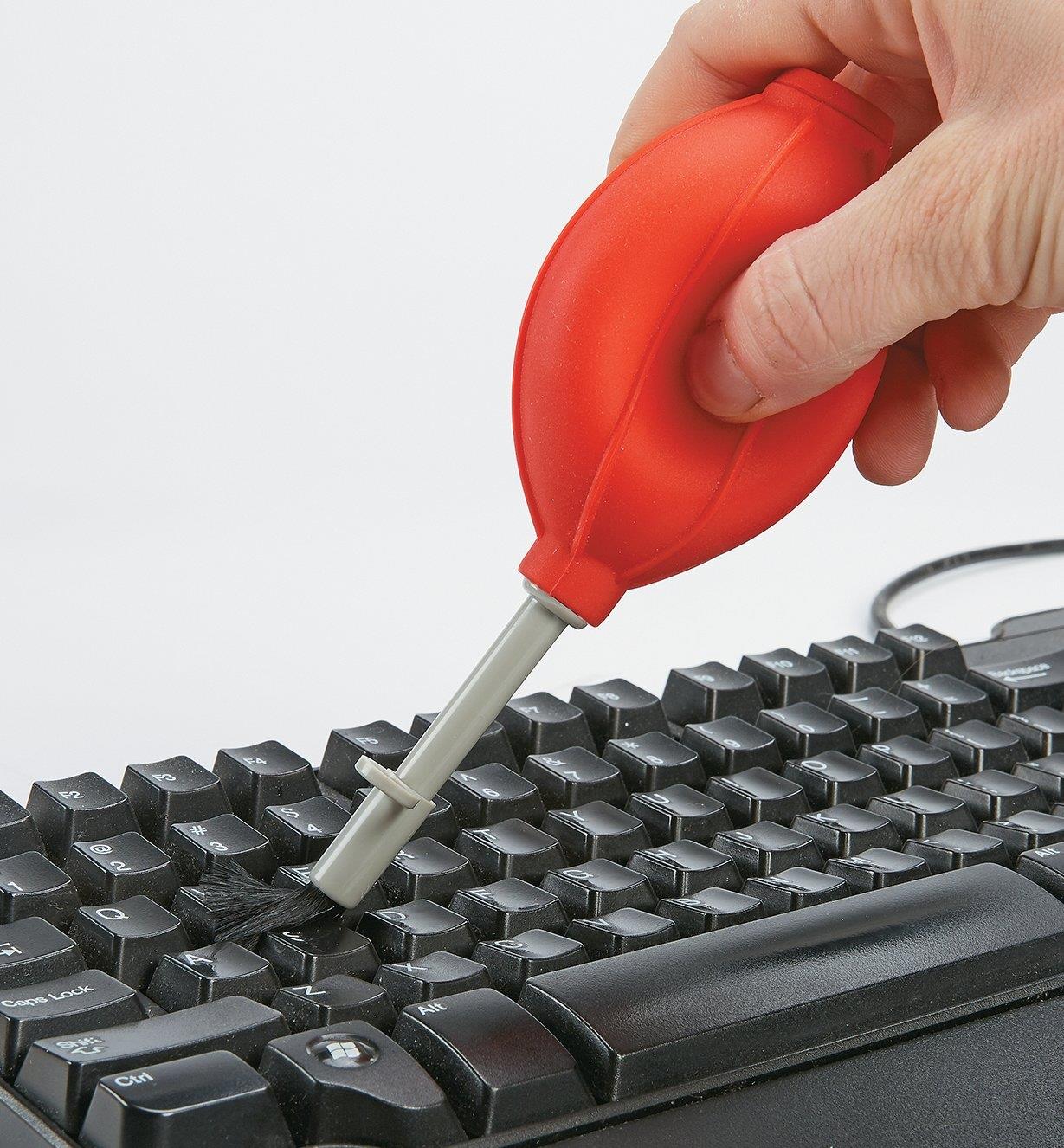 Personne utilisant une poire soufflante en silicone pour nettoyer un clavier