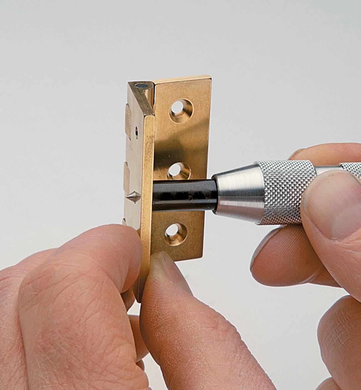 Inserting the Hinge-Locating Punch into the screw hole of a hinge