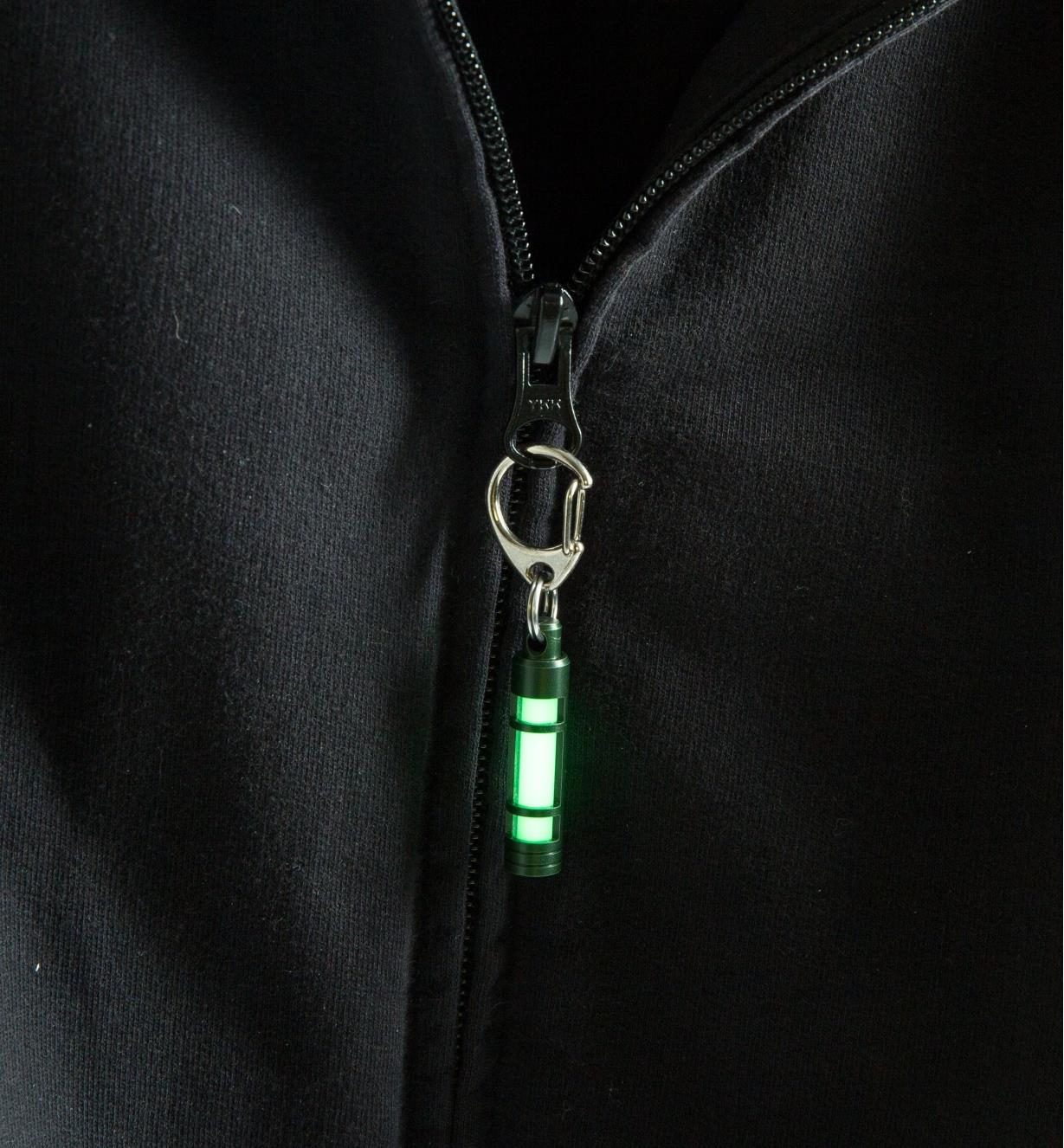 TEC Glow Fob hanging from a sweatshirt zipper, glowing in the dark