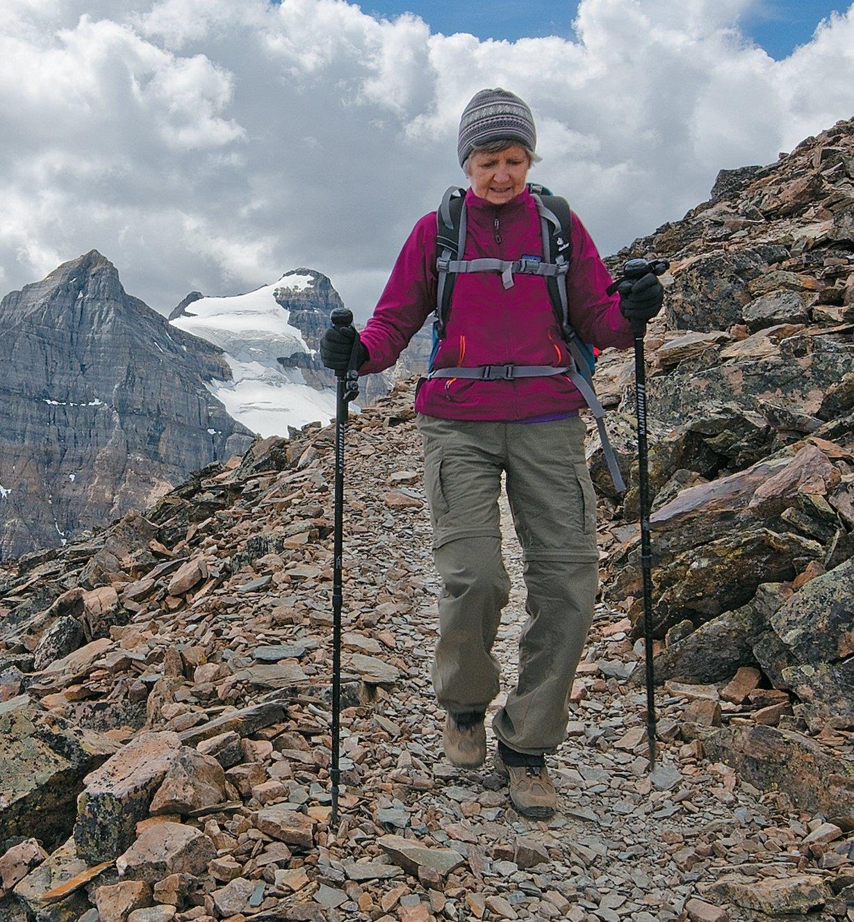 A woman hikes in the mountains with the aid of two telescoping hiking sticks