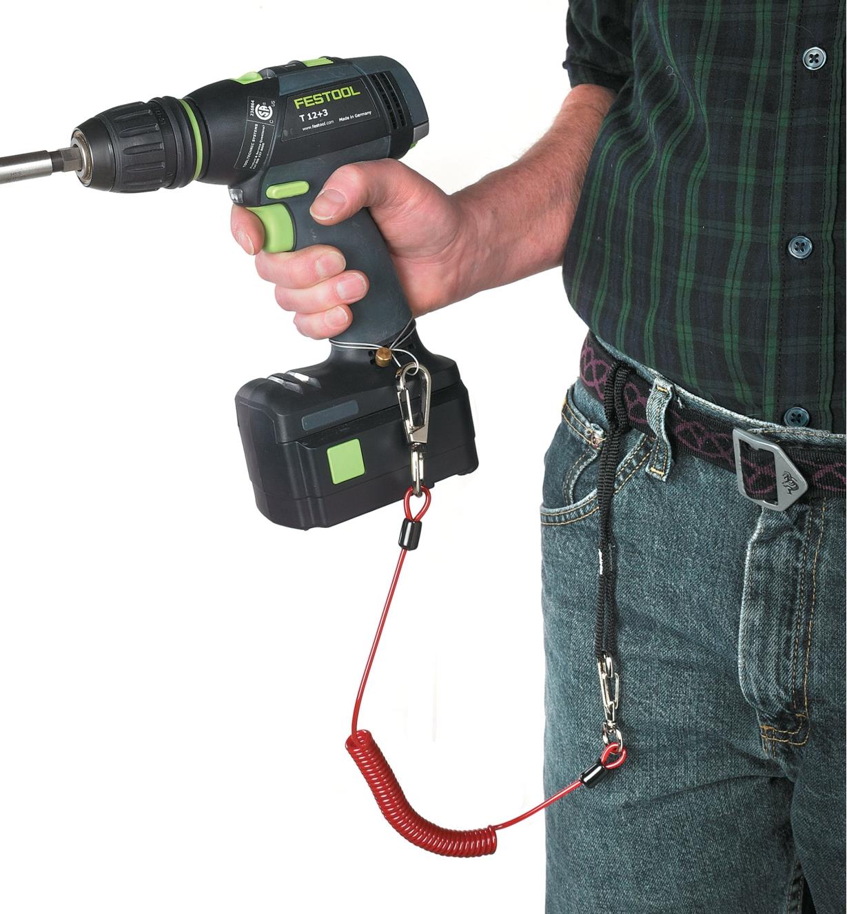 A person holding a cordless drill that is connected to their belt by a tool safety tether