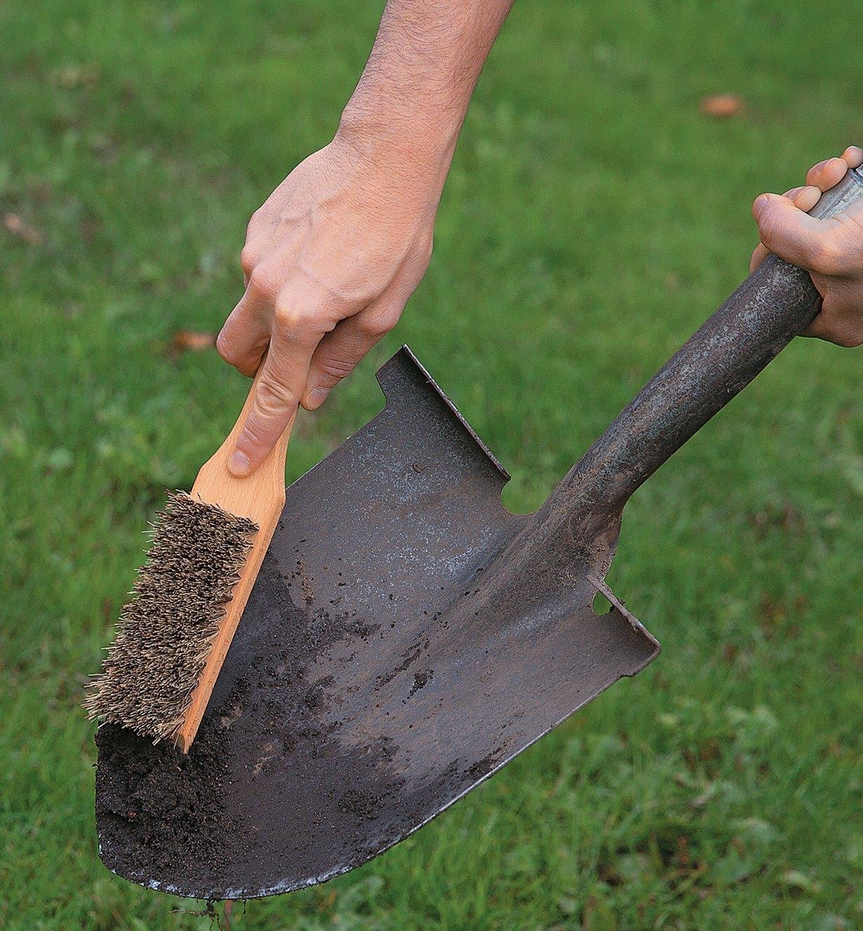 Scraping dirt off a spade using the bevelled end of the Toolshed Brush