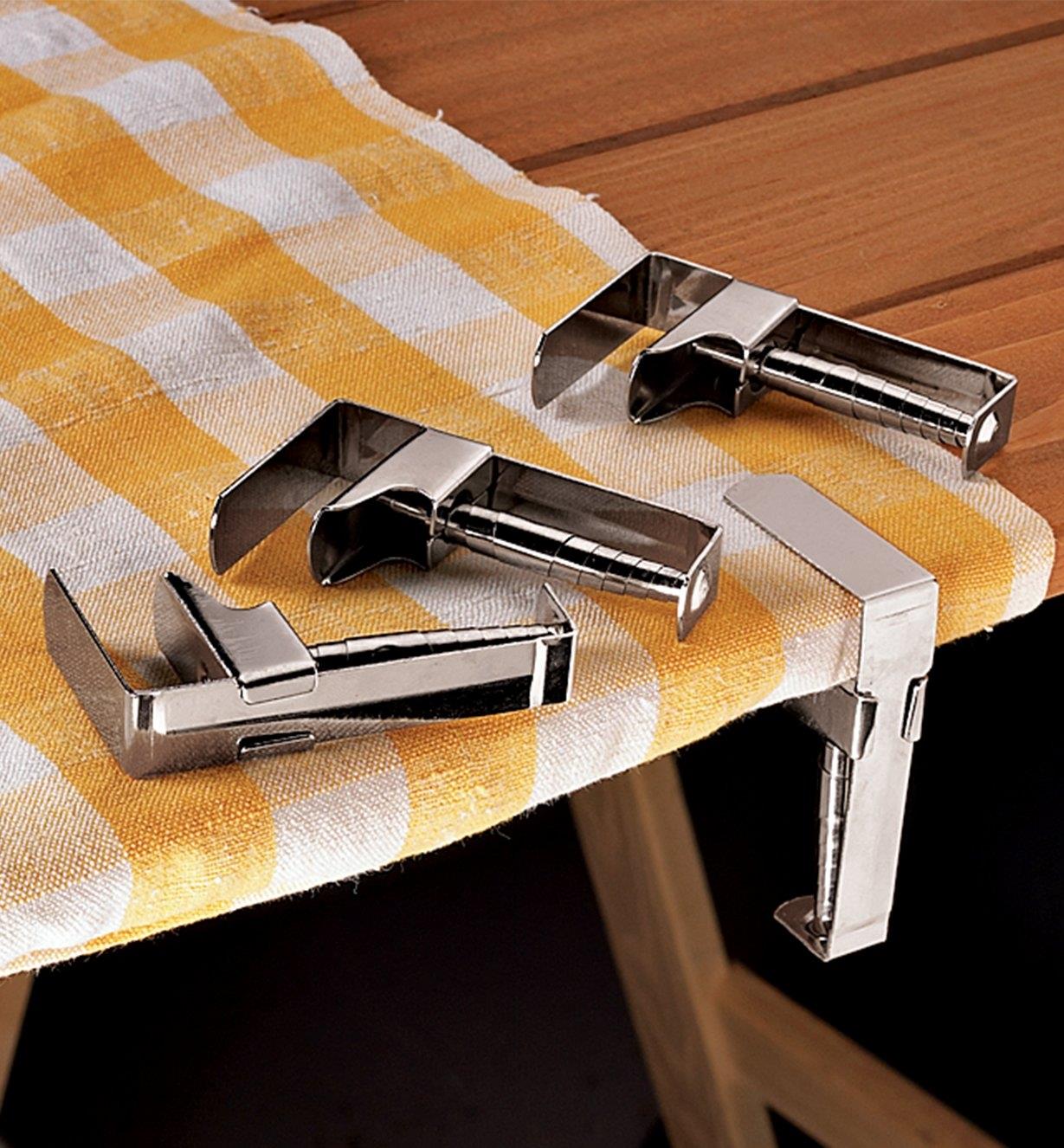 One tablecloth clip holding a tablecloth on a picnic table, and three clips lying next to it 