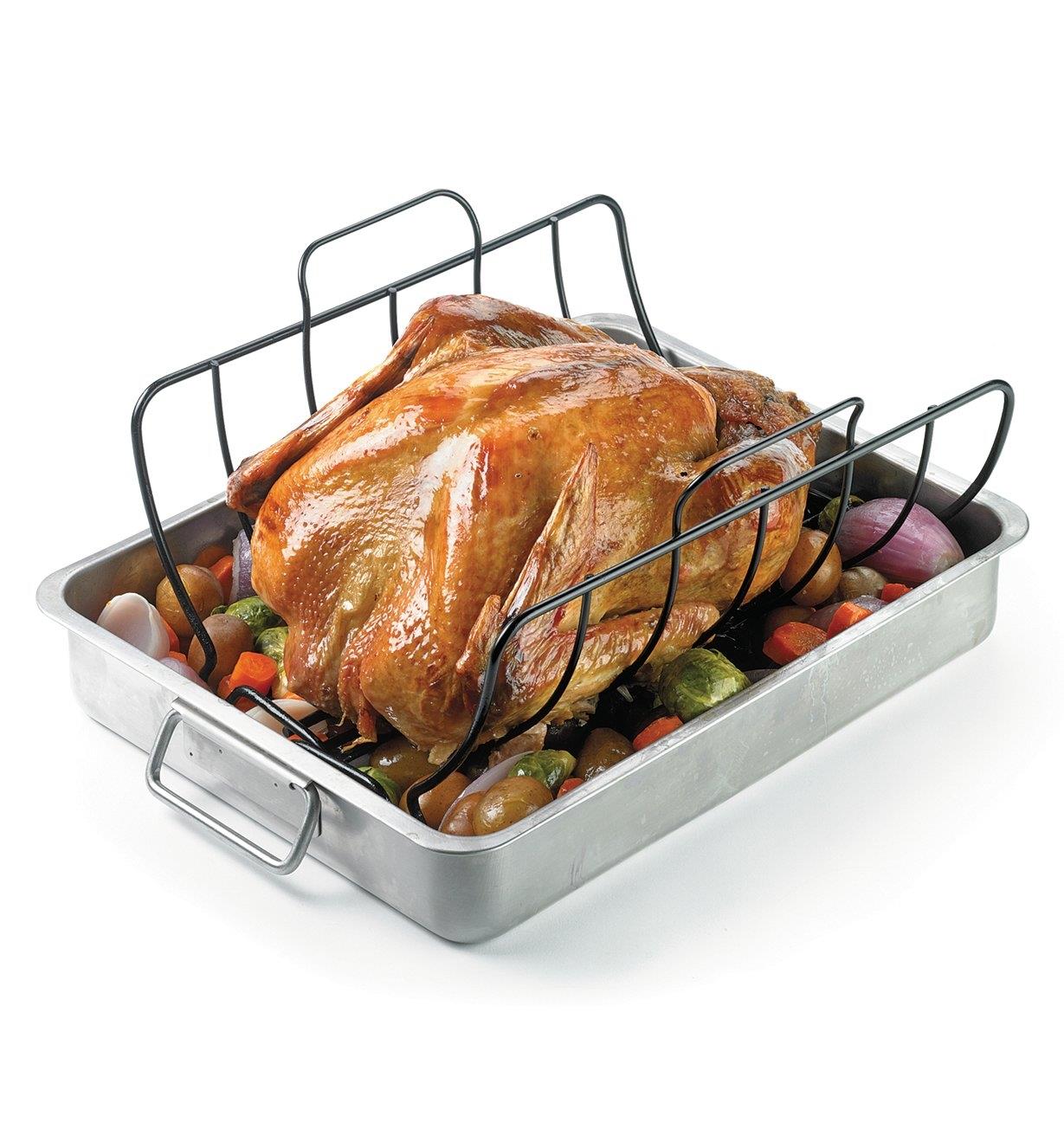 Roast chicken on a roasting rack sitting in a roasting pan with vegetables