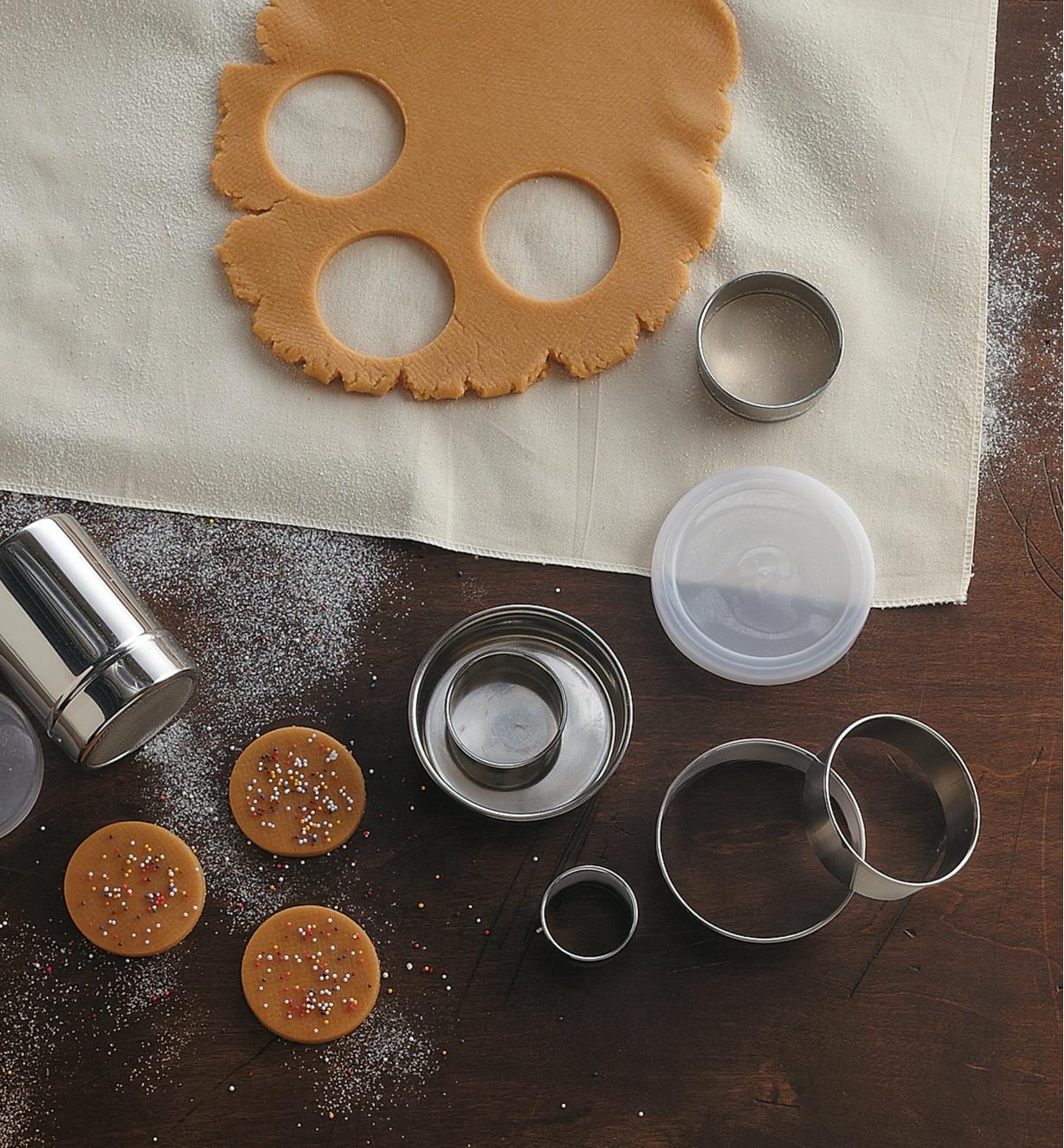 Jeux d'emporte-pièce en acier inoxydable près d'une abaisse de pâte à biscuits et de trois biscuits découpés