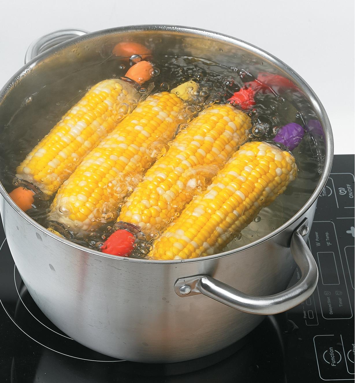 Four cobs of corn with corn holders in a pot of boiling water