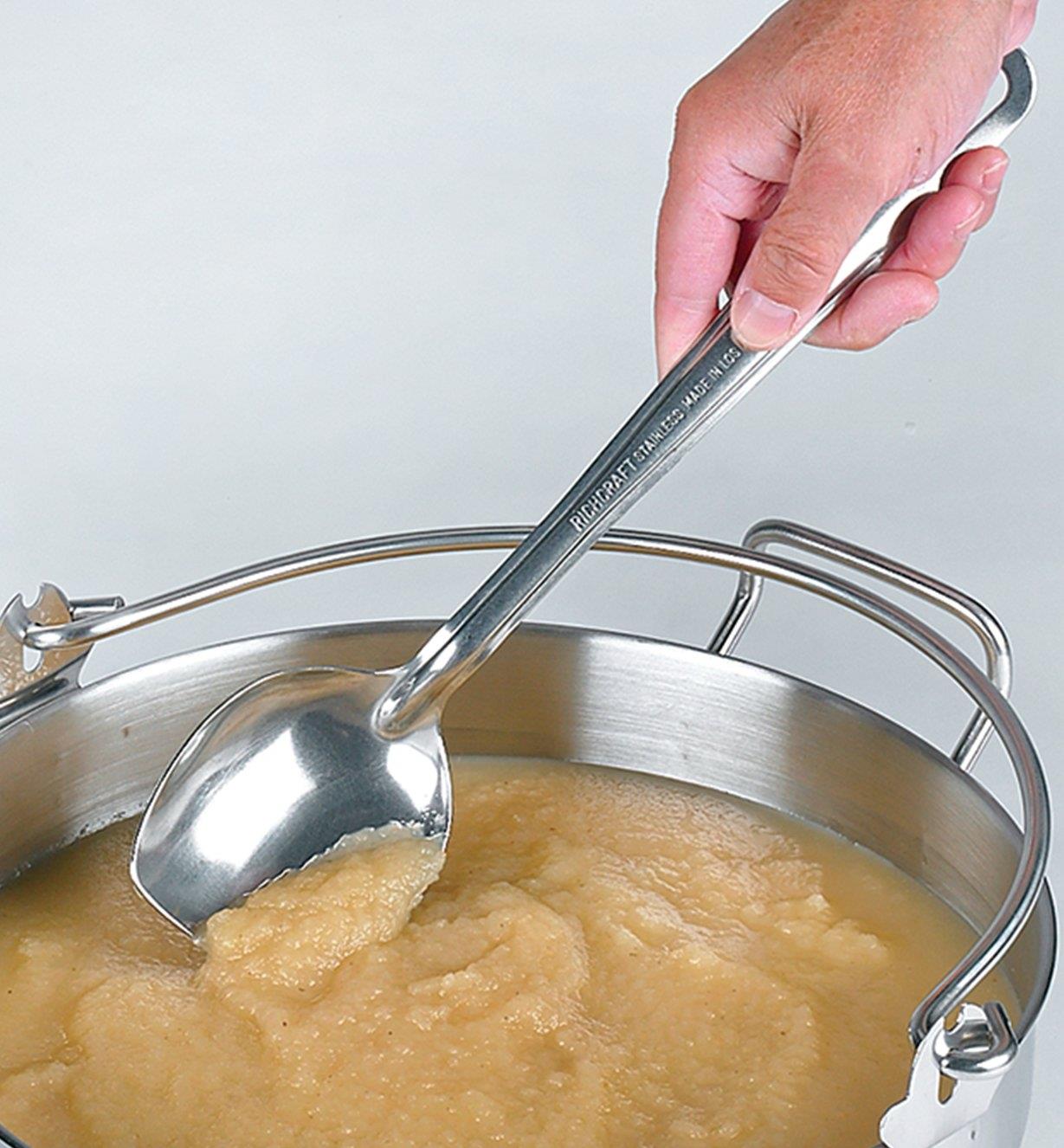 Using the solid slanted spoon to stir apple sauce in a pot
