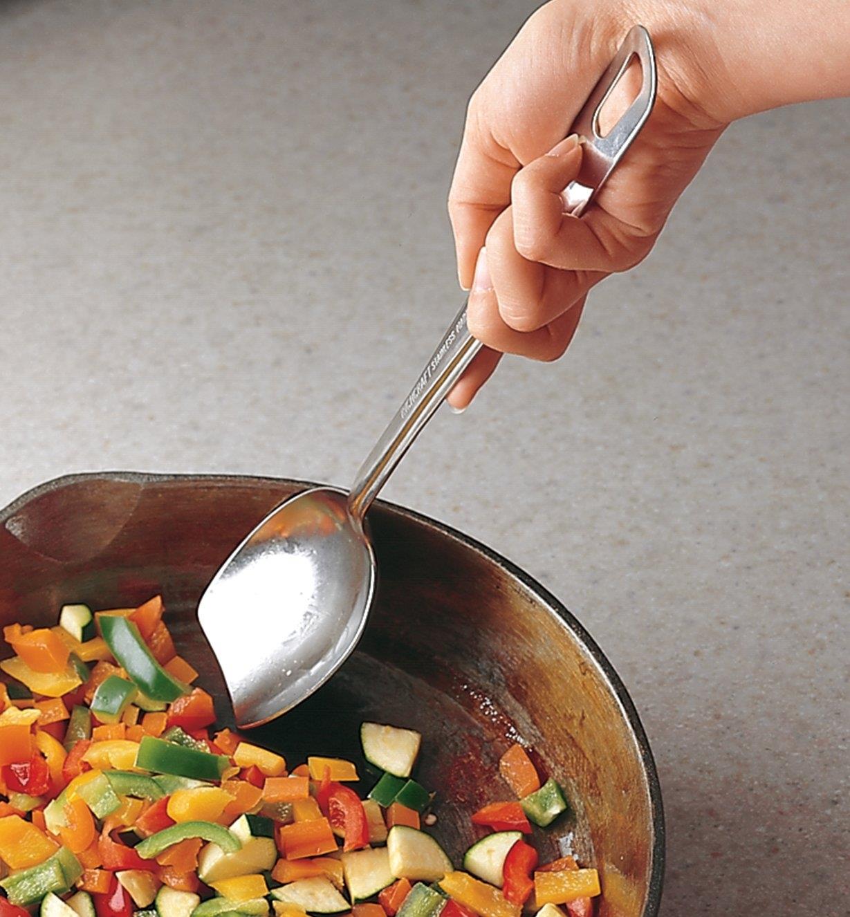 Using the solid slanted spoon to stir diced vegetables in a frying pan