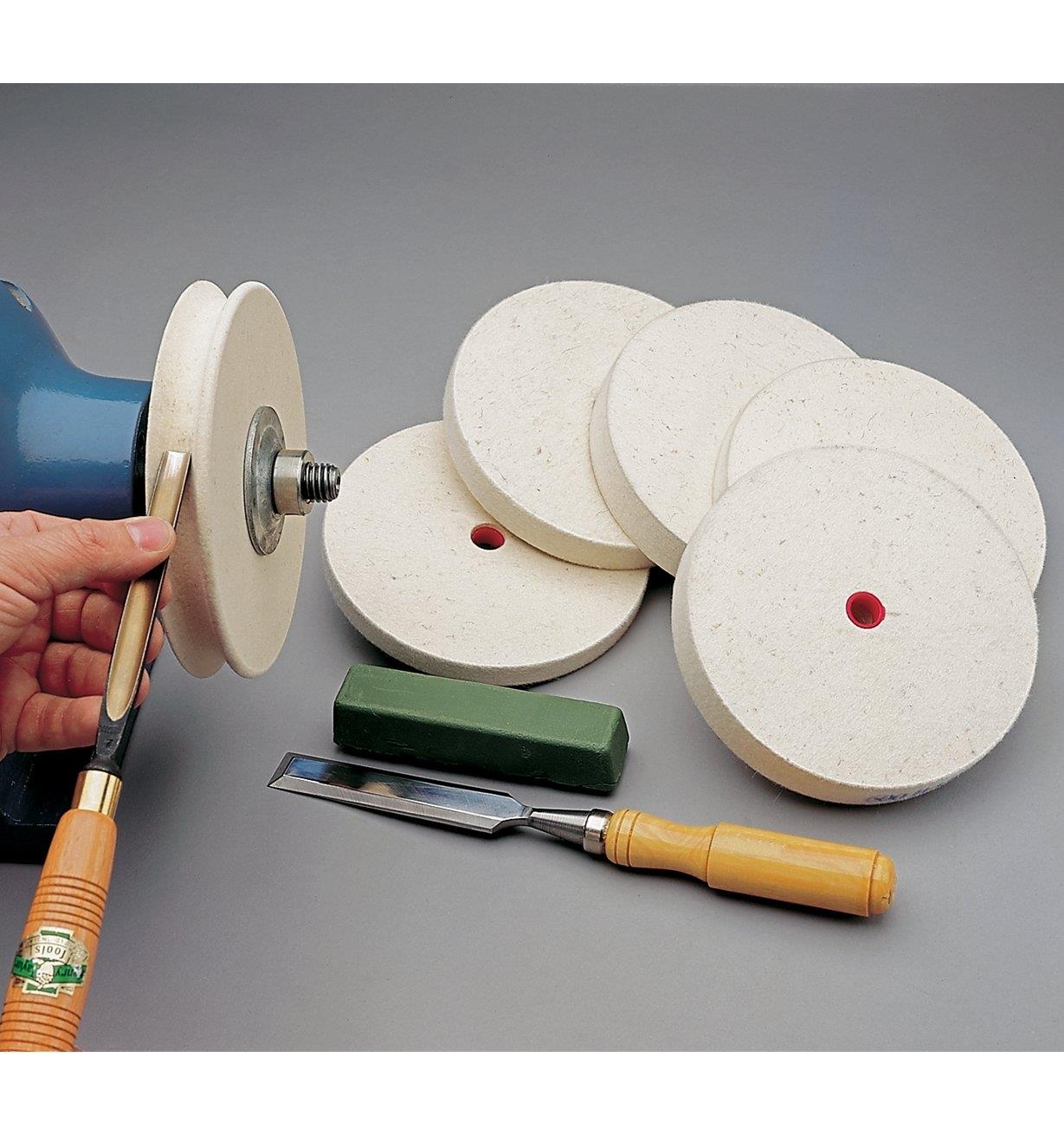 Honing a gouge on a shaped felt wheel, next to a pile of felt wheels, a chisel and a bar of honing compound