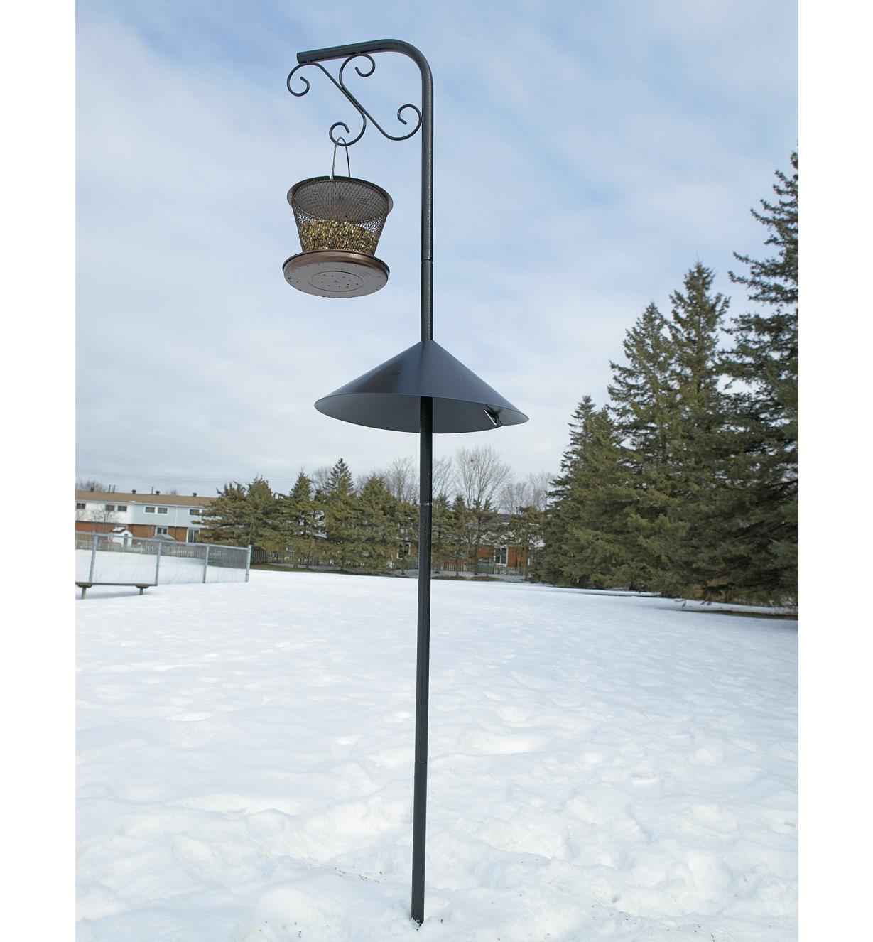 Wrap-Around Squirrel Baffle mounted on a garden hanger holding a bird feeder in winter