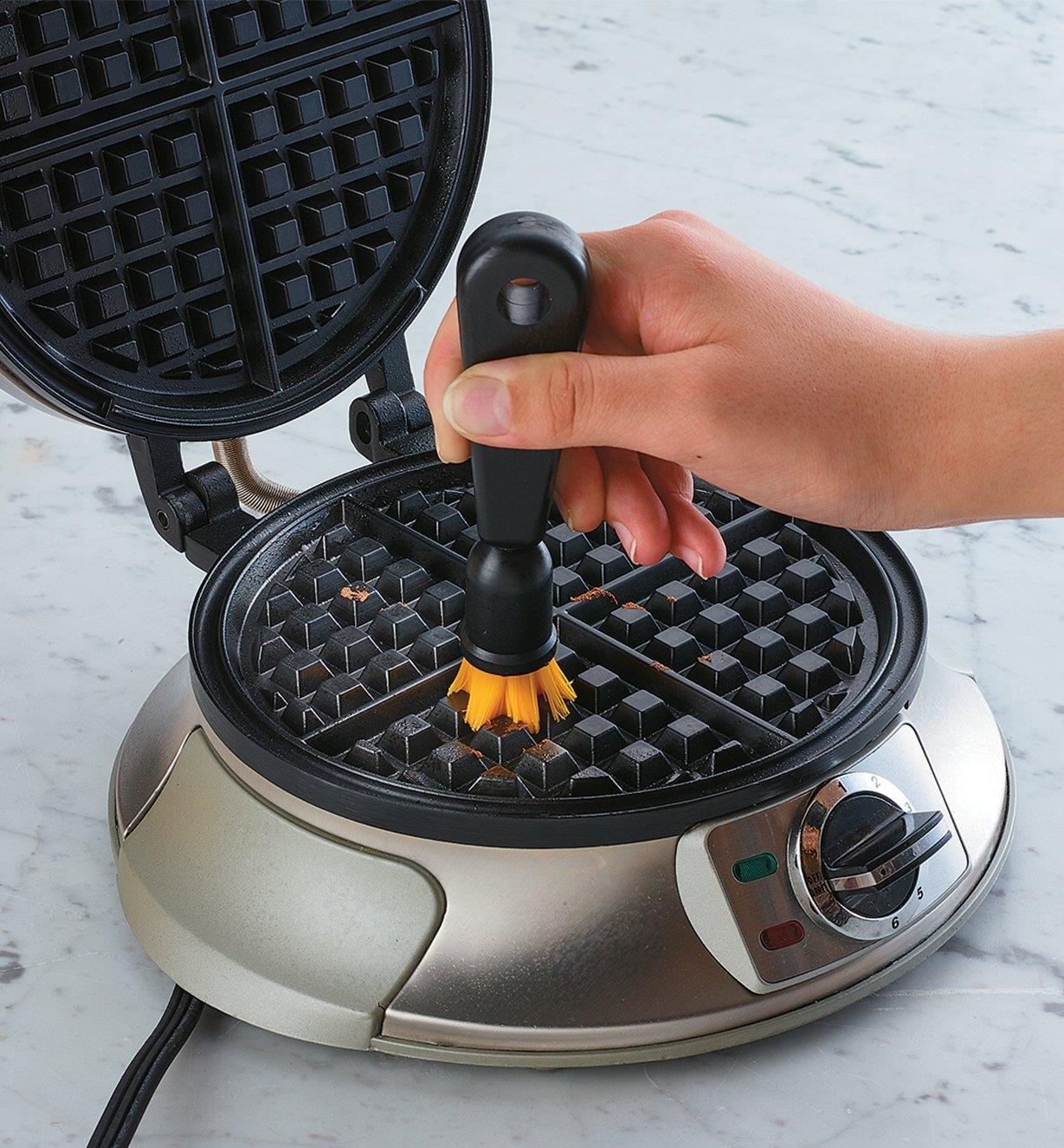 Using the brush with plastic bristles to clean a waffle iron