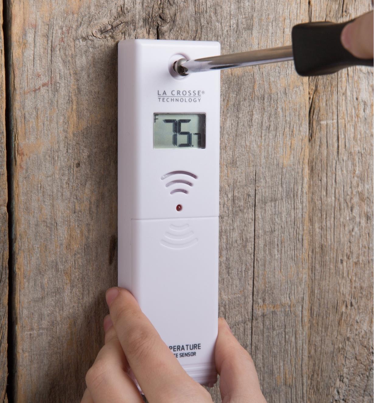 Personne vissant un thermomètre extérieur sans fil à un mur