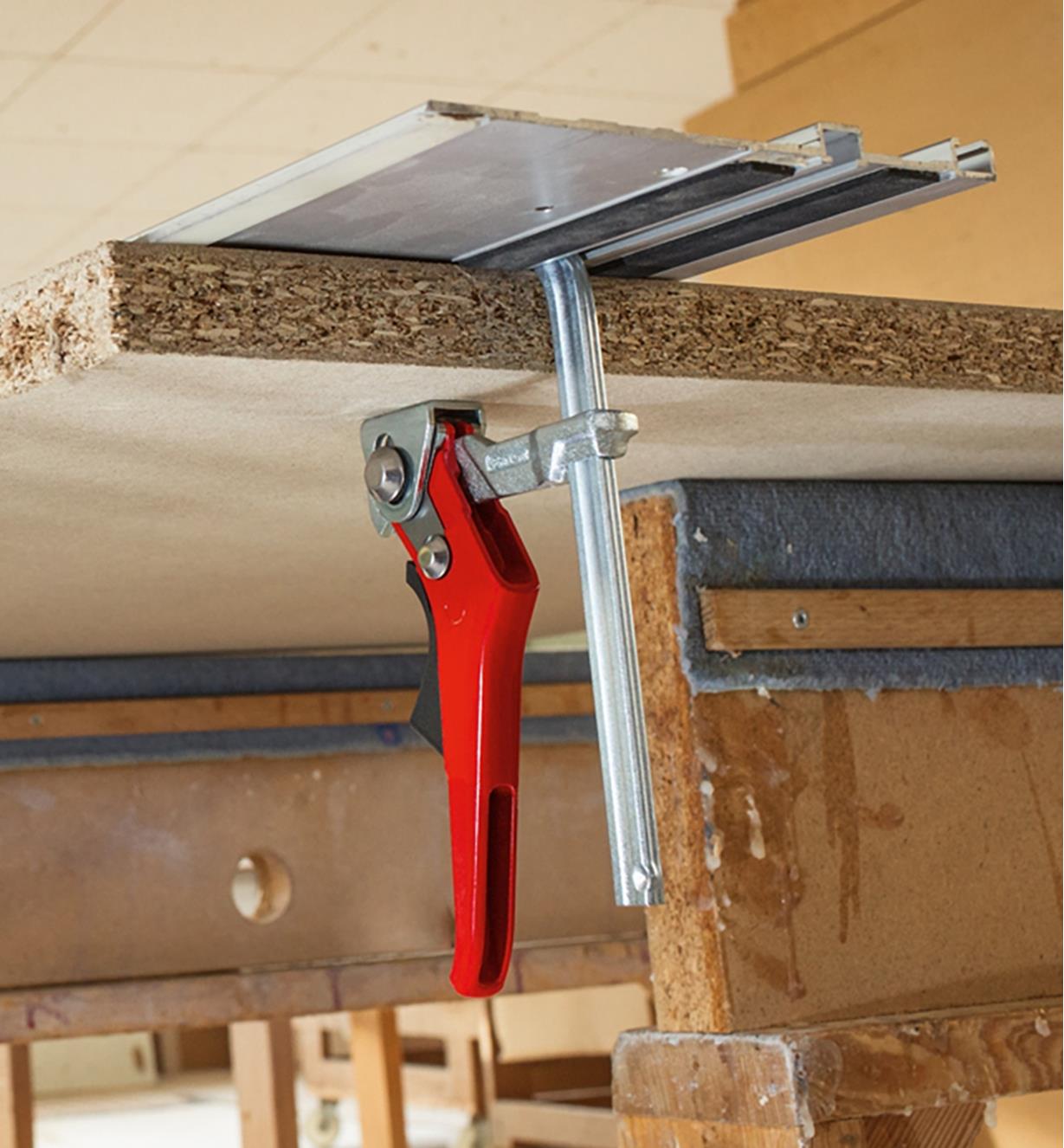 A Bessey ratcheting track clamp being used to hold a track-saw guide in position on a panel