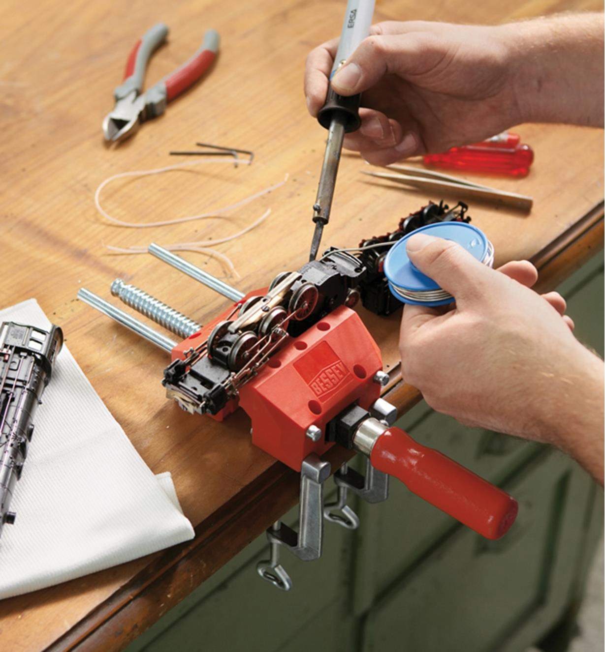 A Bessey portable hobby vise mounted to a table top, holding a model train being repaired