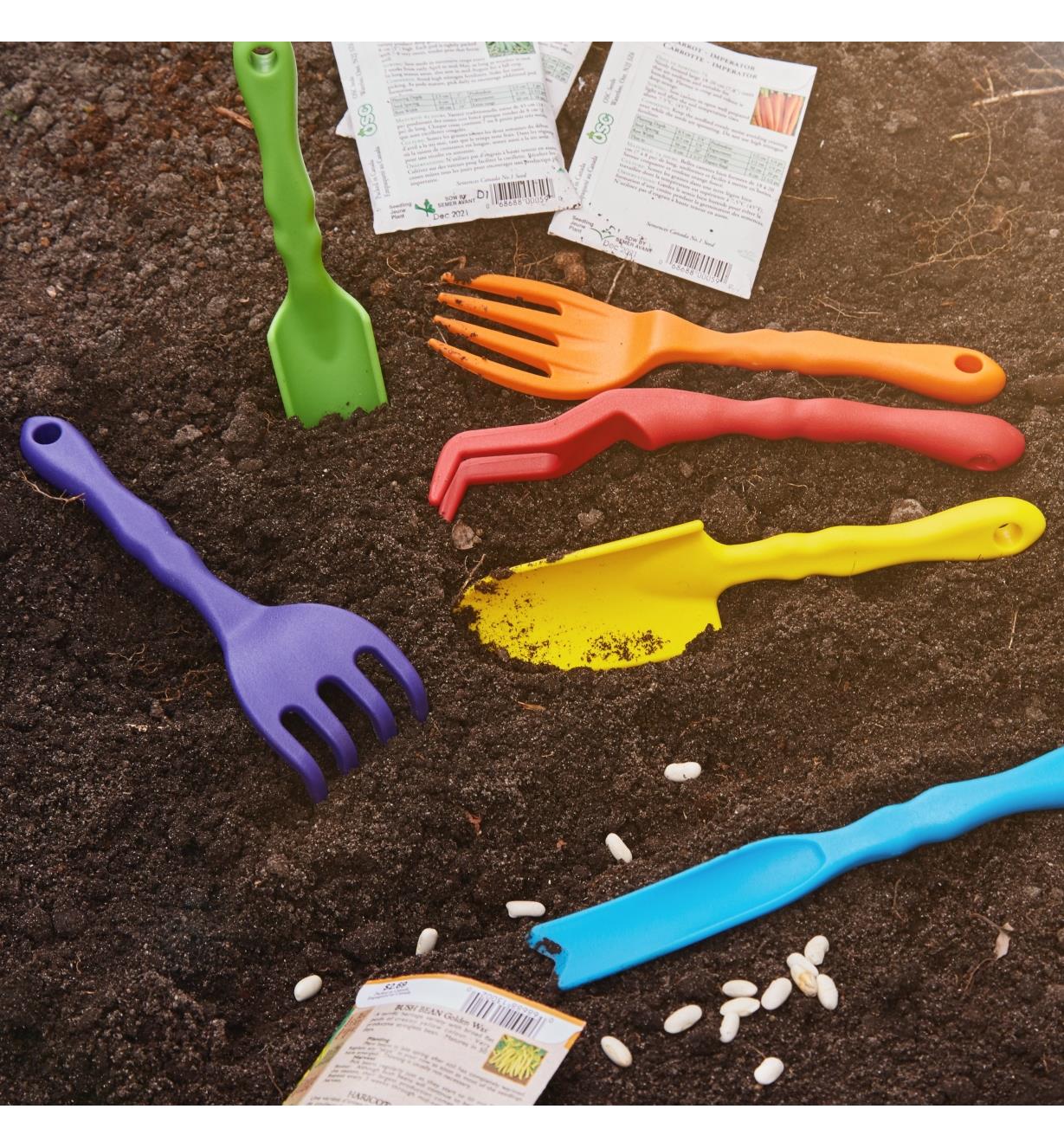 Six outils de jardinage pour enfants dans une plate-bande près de graines prêtes à planter