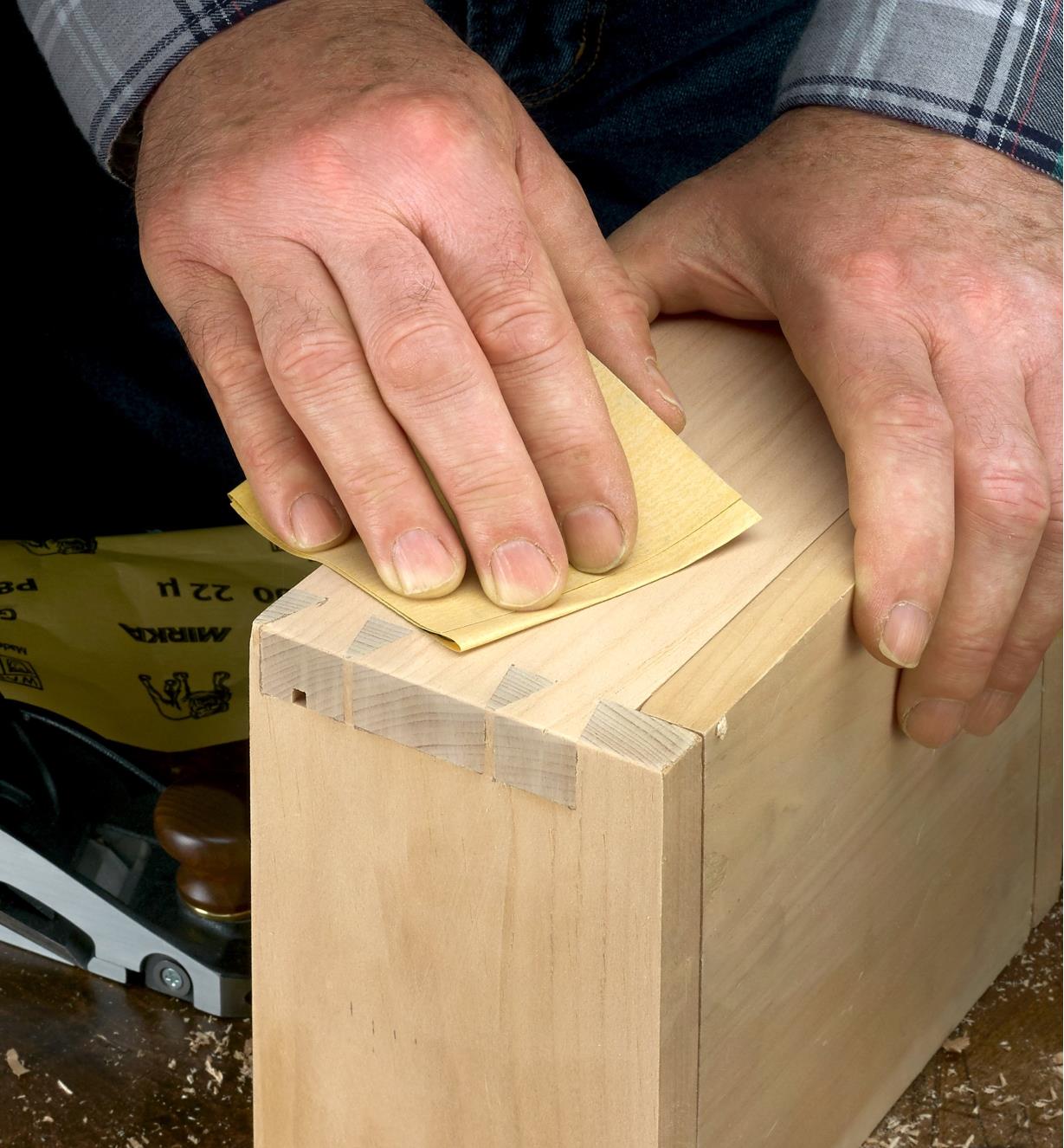 A woodworker uses Mirka Gold sandpaper to sand the dovetailed corner of a wooden box