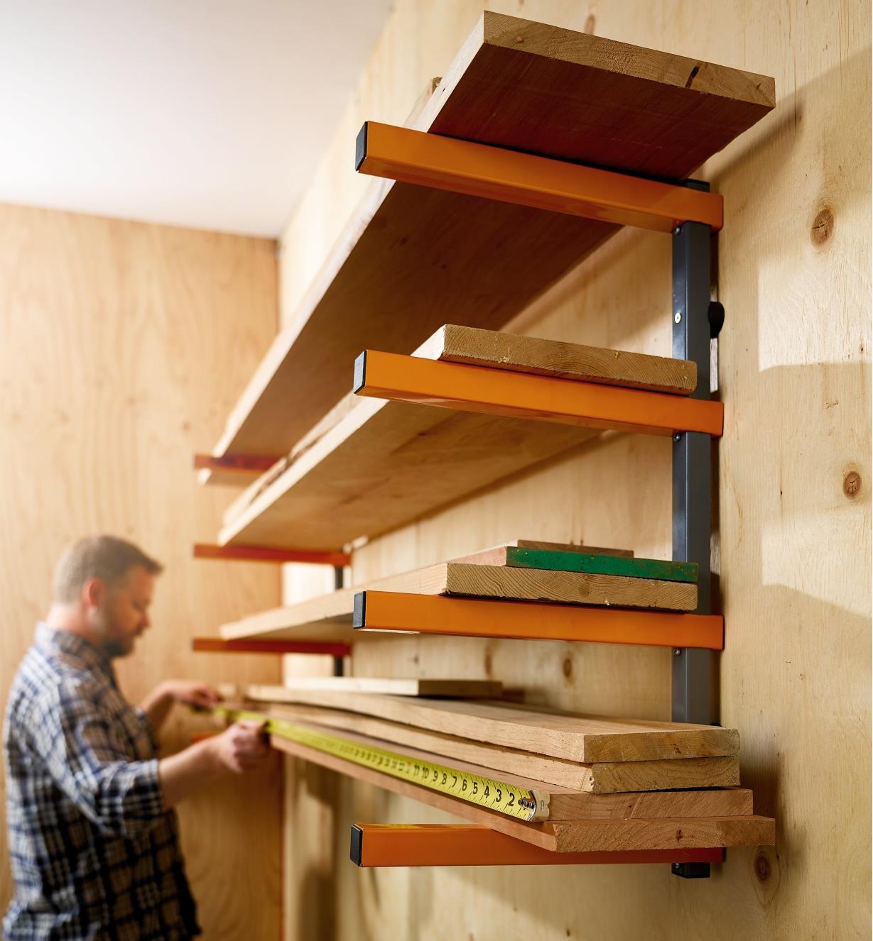A man measures wooden boards stacked on a Bora four-shelf lumber rack