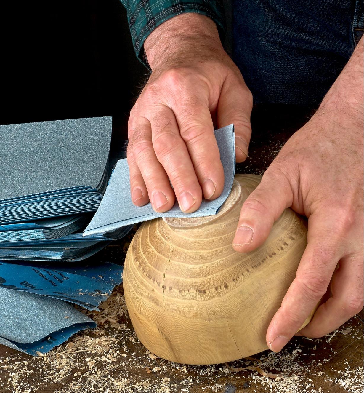 A woodworker sands a turned wooden bowl with a sheet of Norton ProSand 3X Sandpaper