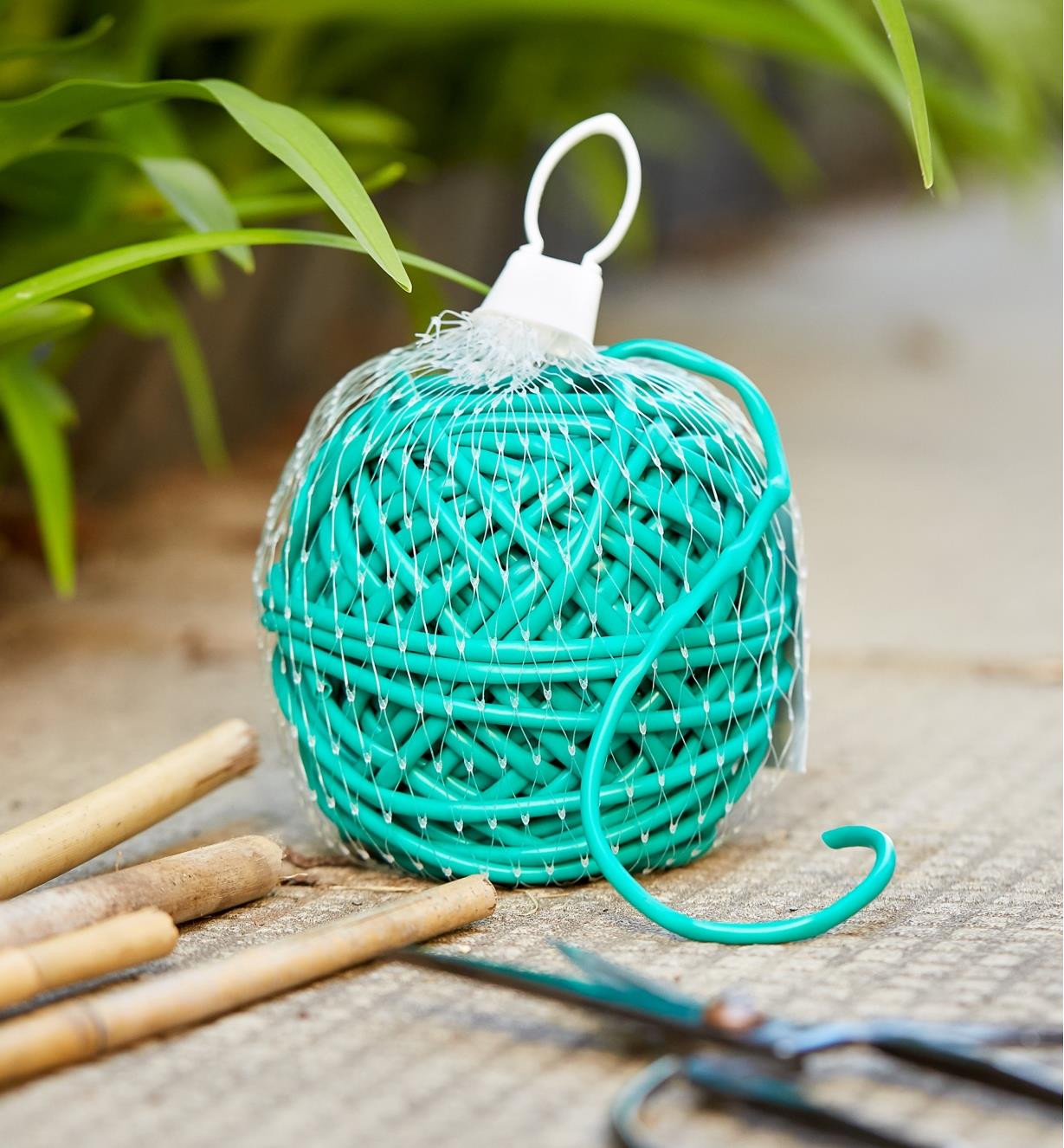 A 100' bundle of soft-stretch plant tie shown with bamboo garden stakes and a pair of scissors