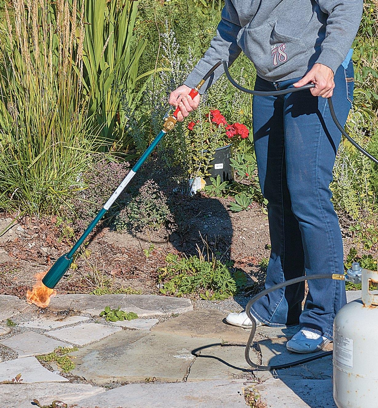 A woman uses the Giant Weed Torch to remove weeds from a walkway