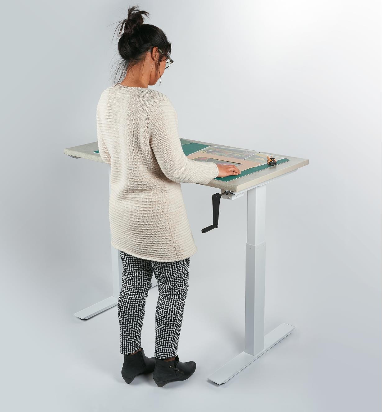 A woman standing works at a table made with the Manual Table Lift Kit