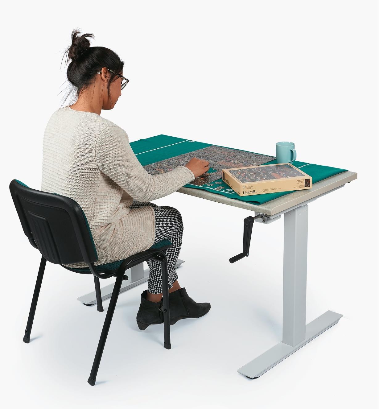 A woman sitting in a chair works on a jigsaw puzzle at a table made with the Manual Table Lift Kit