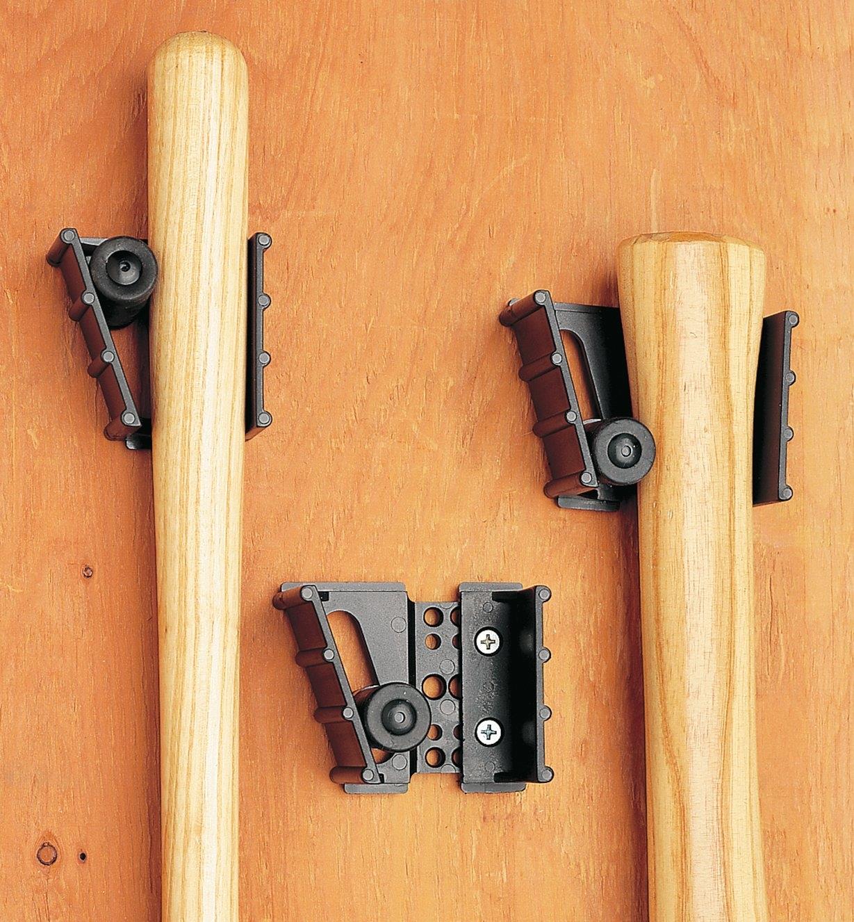 Three Adjustable Gripits attached to a wall, two of them holding tool handles