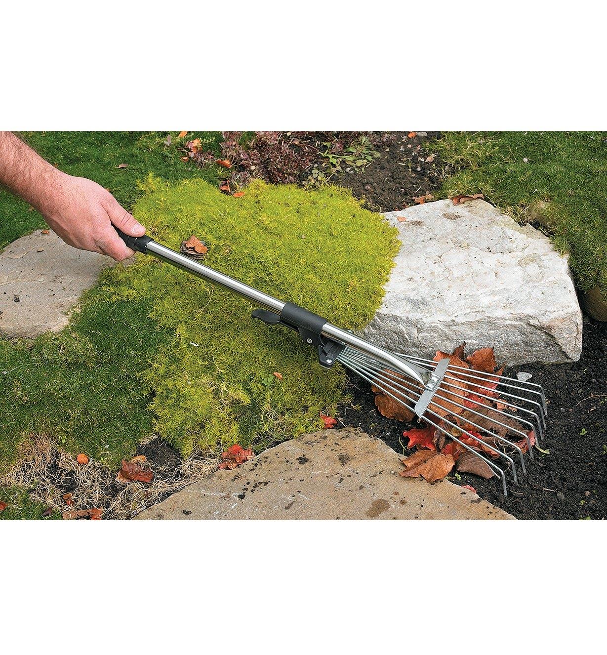 Balai à feuilles à manche court utilisé pour ratisser des feuilles autour de roches dans un jardin