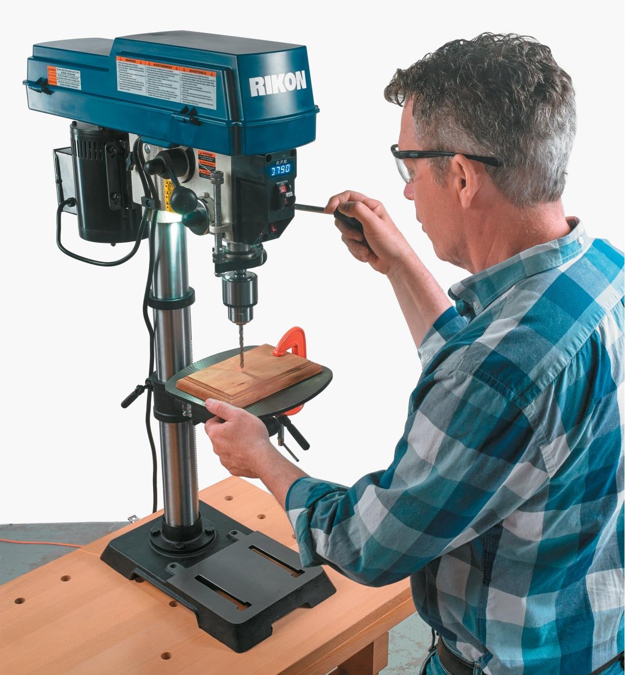 A man uses the drill press to drill a hole in a board