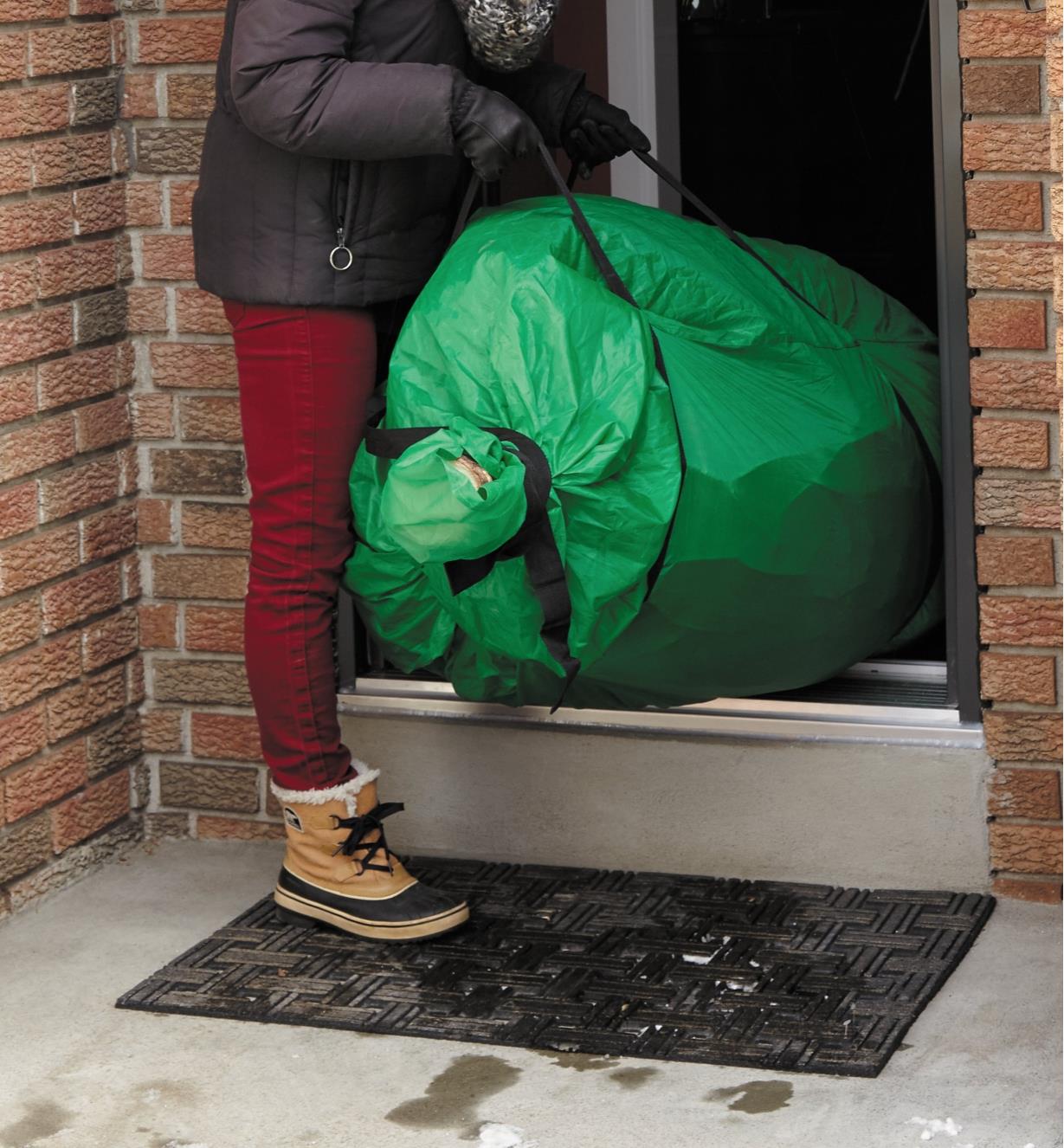 A woman carries a tree out the door using the Christmas Tree Transfer Bag