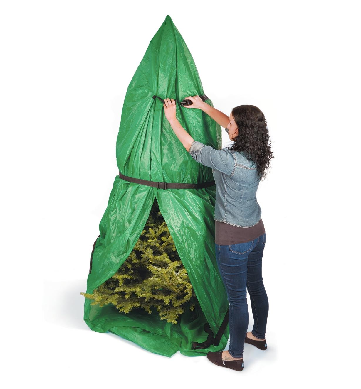 A woman cinches the straps on a Christmas tree transfer bag wrapped around a tree that is standing up