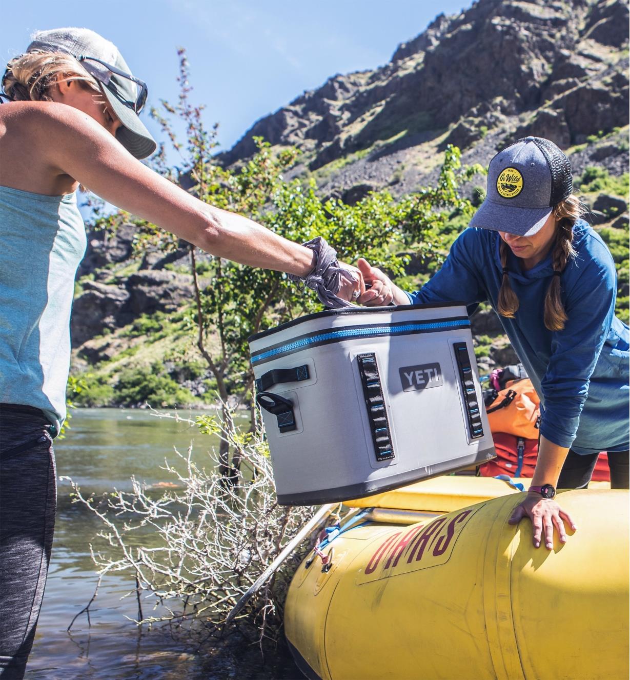 A man and woman load a Yeti Hopper cooler into a raft