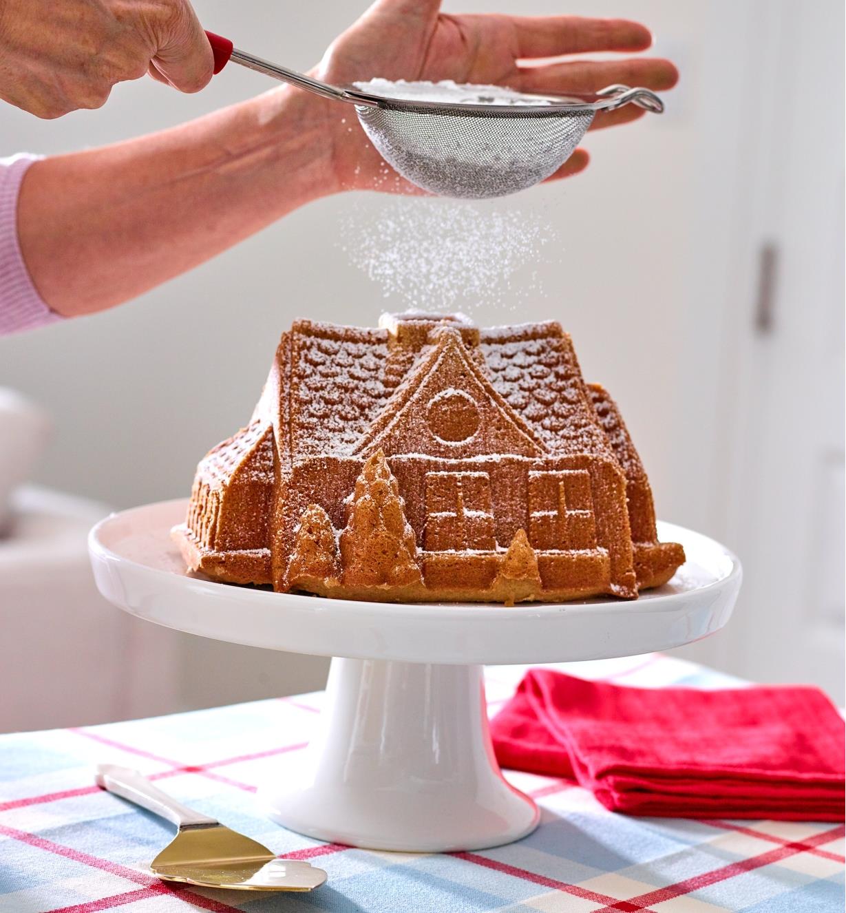 Dusting powdered sugar onto a gingerbread house cake