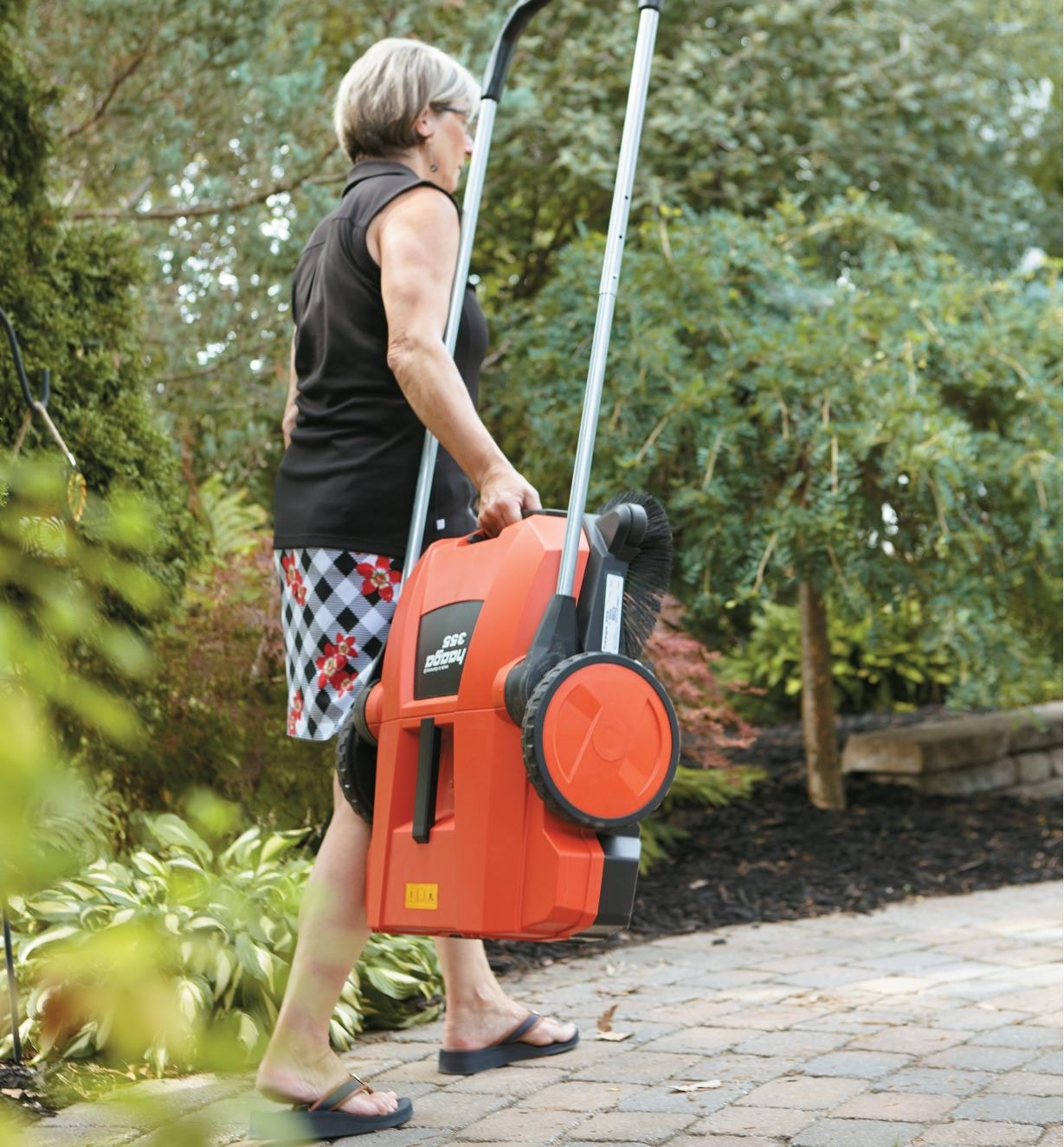 A woman carrying Dual Brush Sweeper with the handle folded