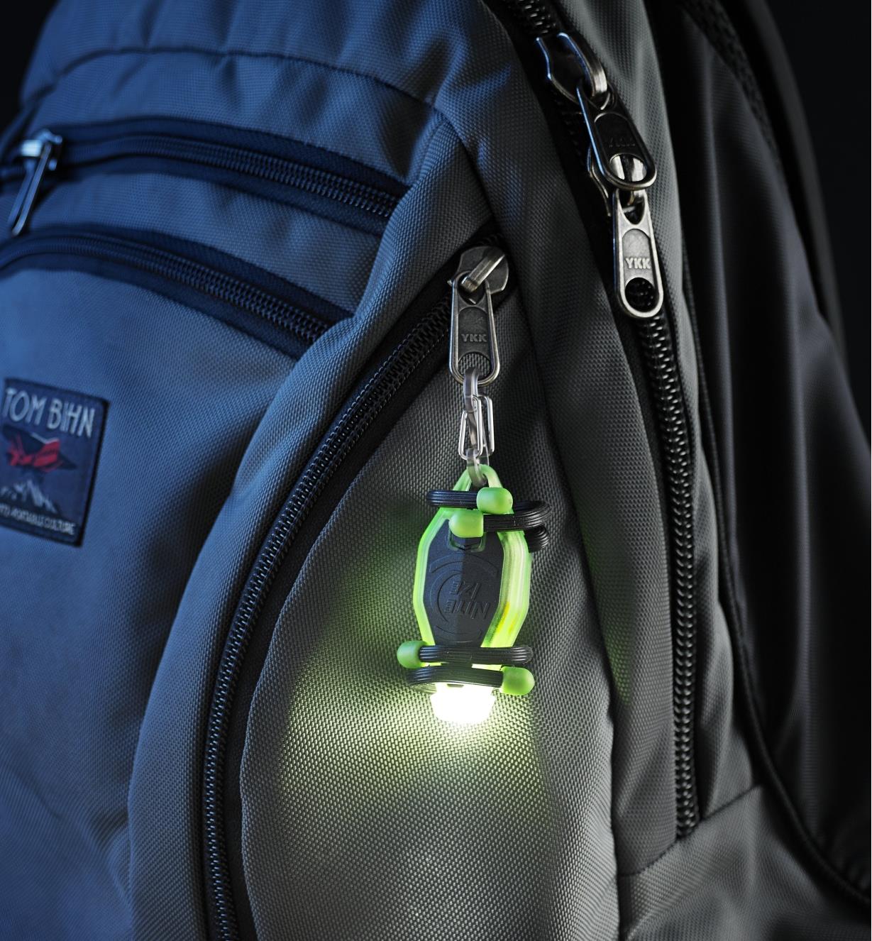 A BugLit rechargeable flashlight hung by the included carabiner on the zipper tab of a backpack