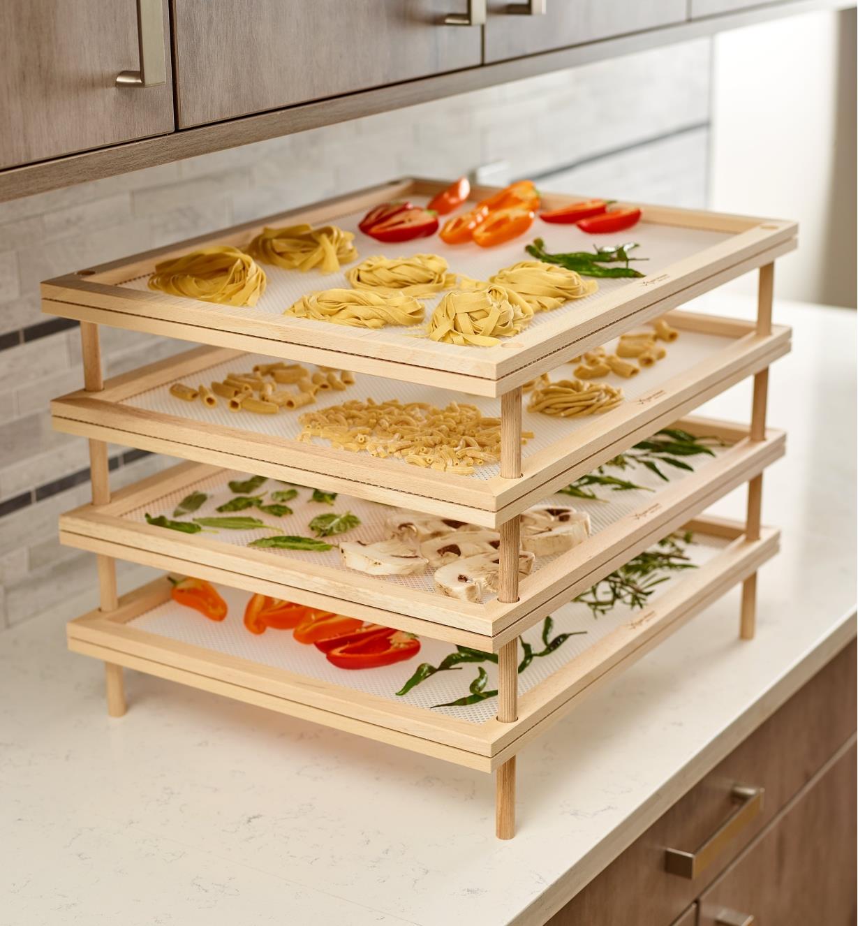 Stack of four mesh trays with pasta and vegetables drying on them