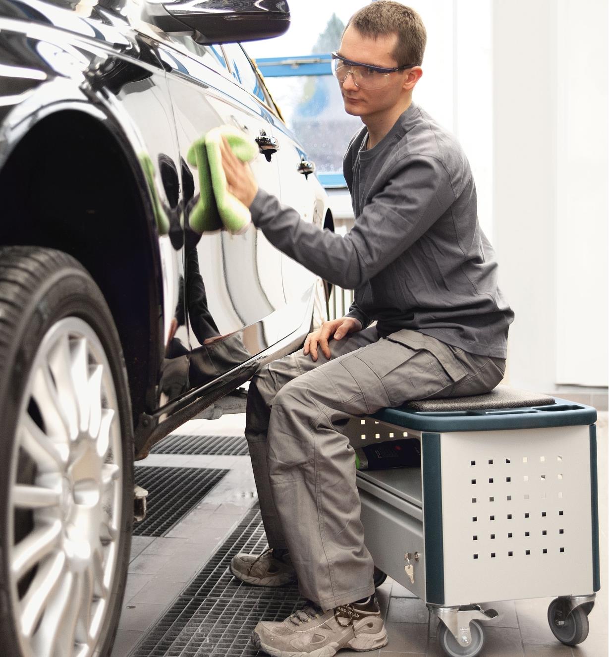 Man sitting on the MMFH 1000 multifunction stool while wiping a car