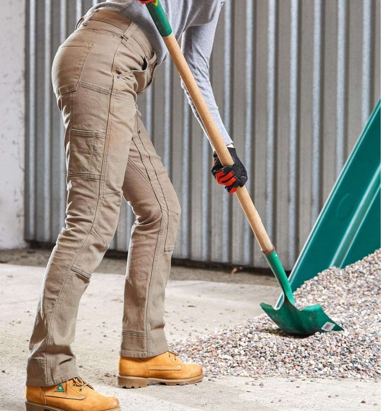 A woman wearing Dovetail pants shovels gravel